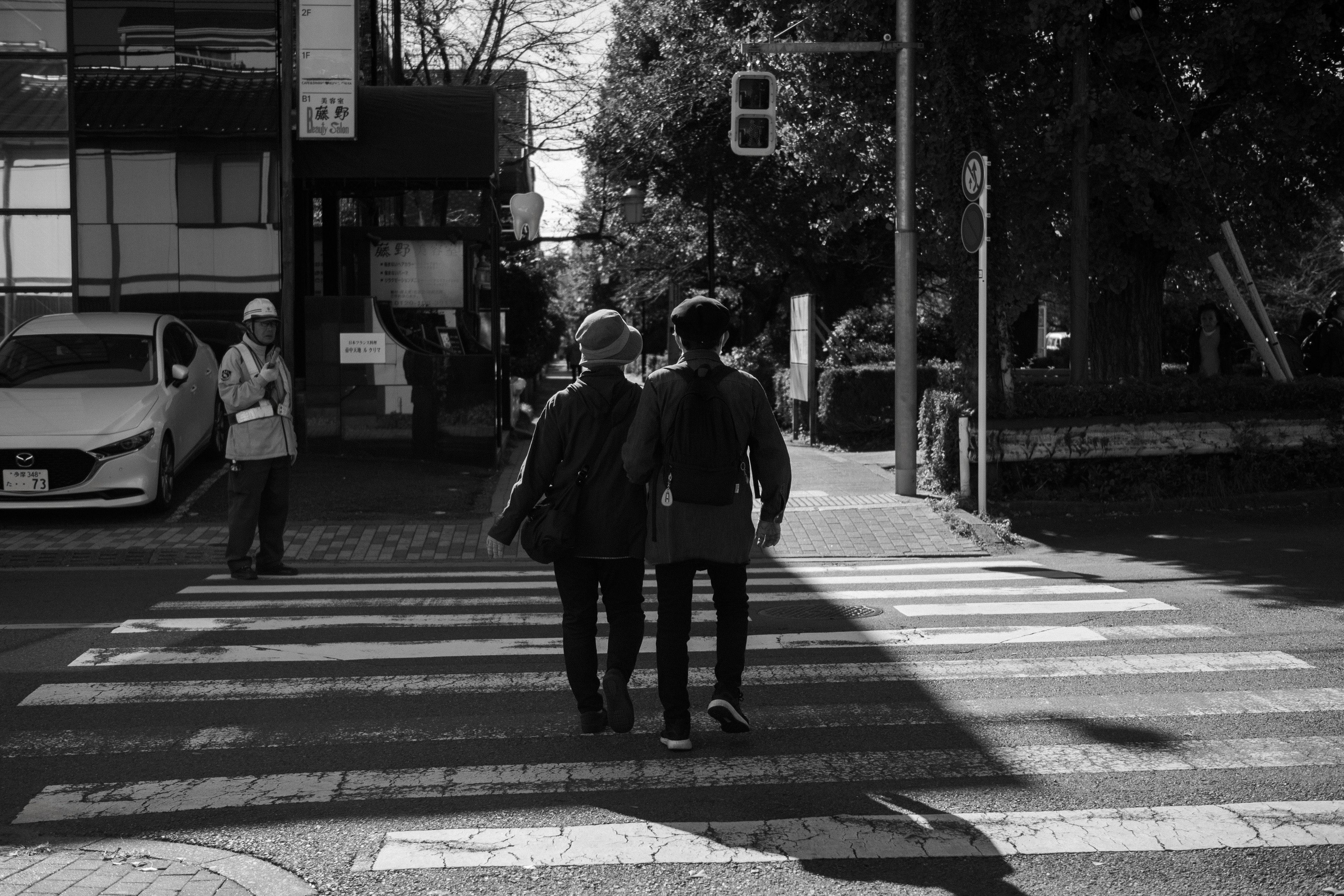 Deux personnes marchant sur un passage piéton en noir et blanc avec des voitures et des bâtiments en arrière-plan