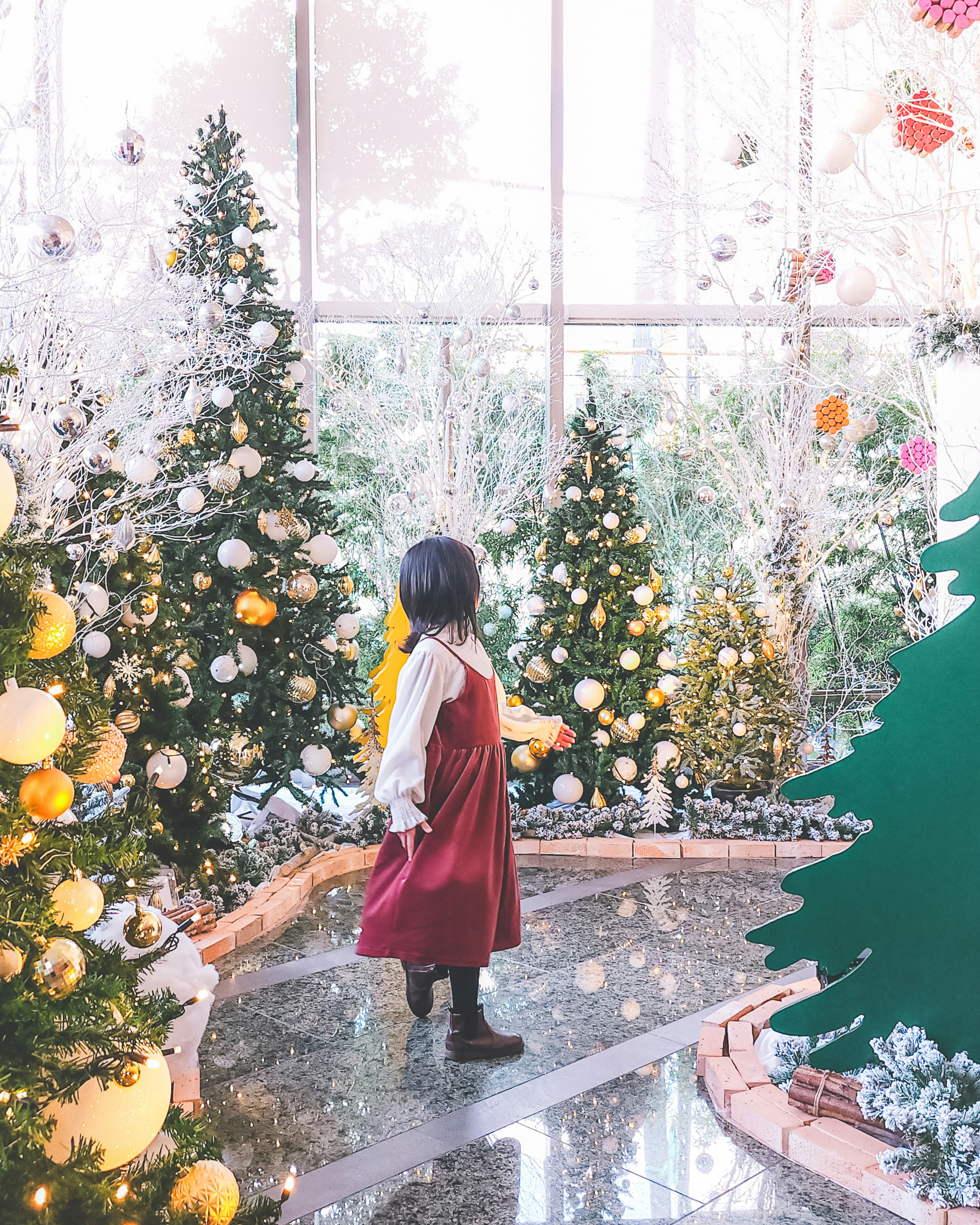 Enfant en robe rouge entouré d'arbres de Noël décorés ornements brillants et ambiance festive