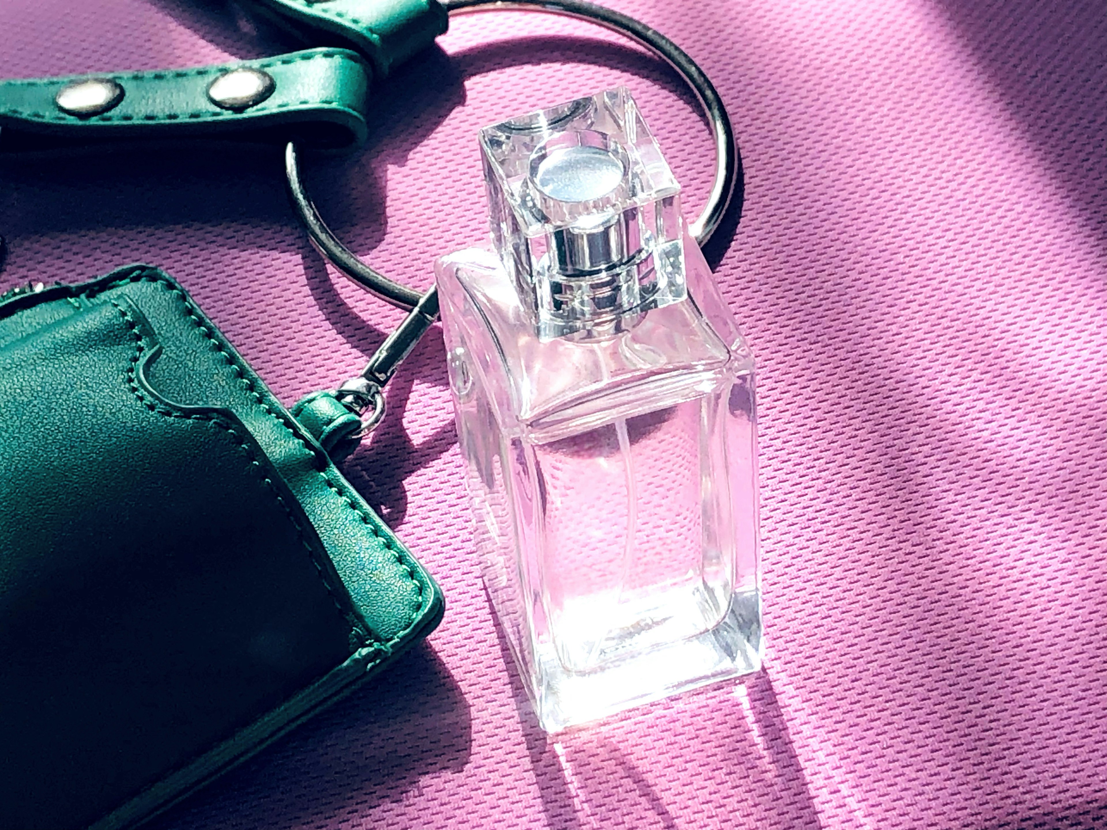 Botella de perfume transparente junto a un accesorio verde sobre un fondo rosa