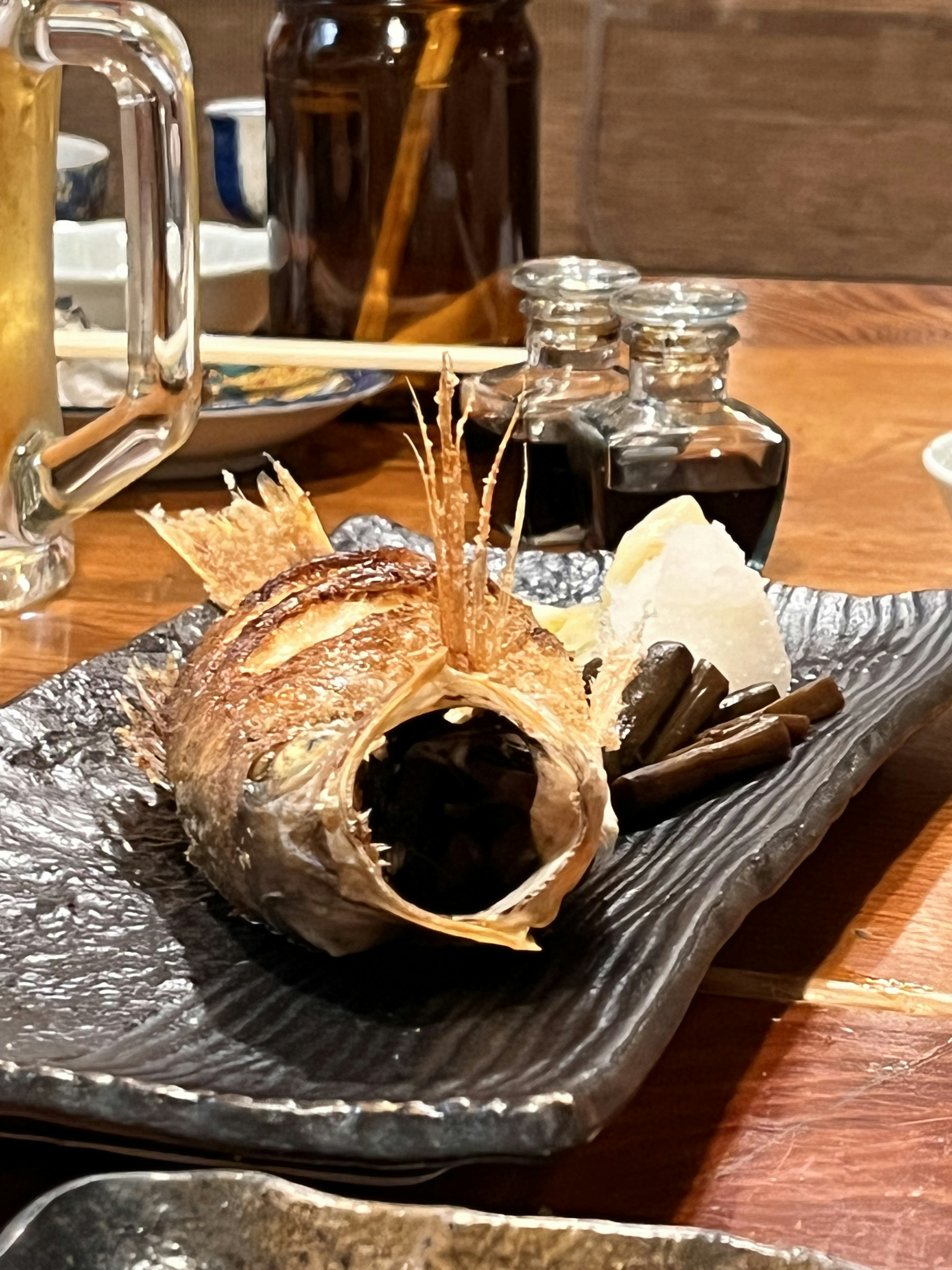 Grilled fish served on a black plate with condiment bottles