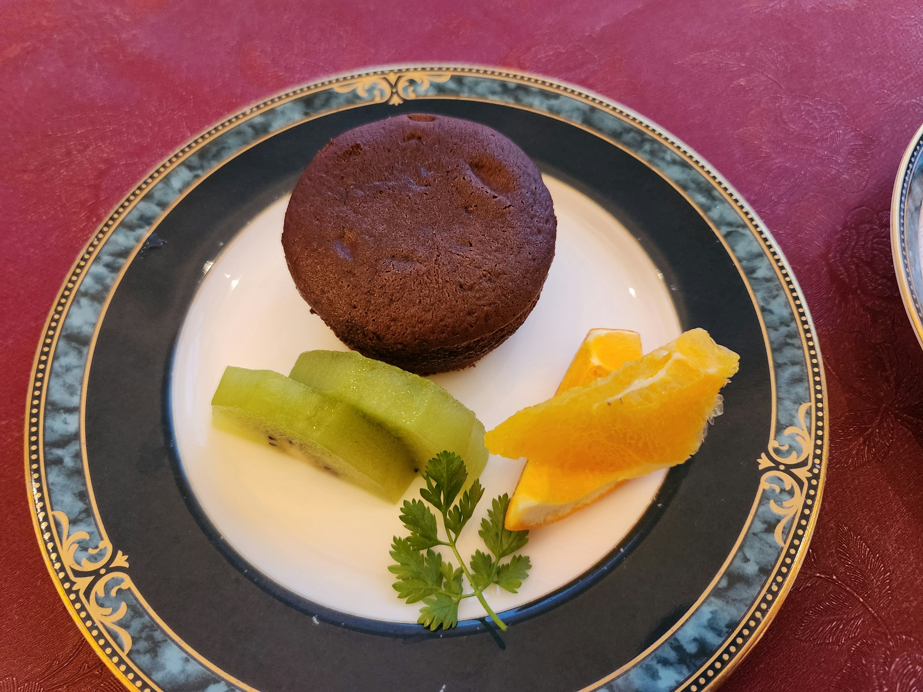 Muffin cokelat disajikan dengan irisan kiwi dan jeruk di piring yang elegan