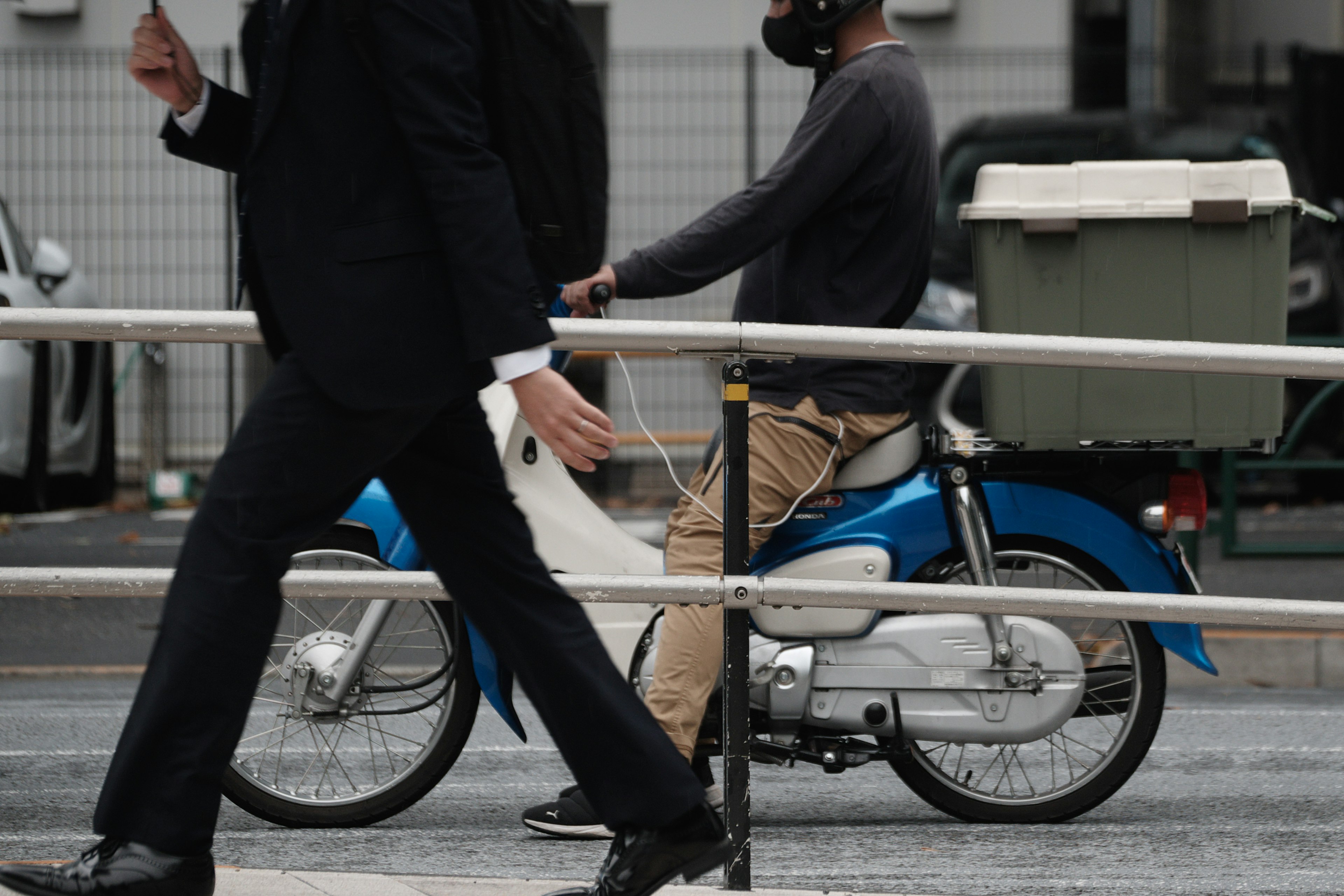 Ein Mann im Anzug geht vorbei, während ein anderer Mann auf einem blauen Motorrad sitzt