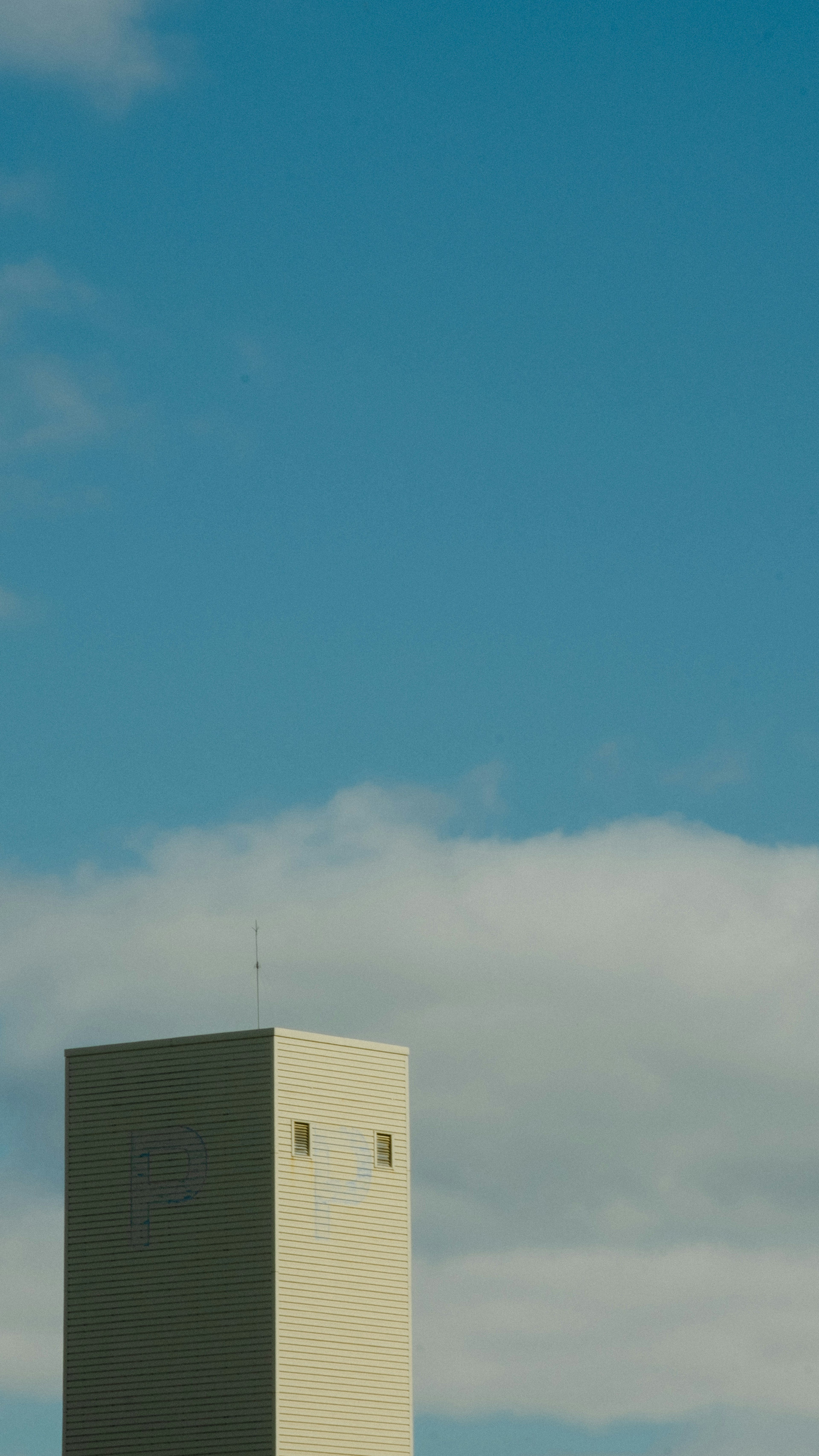 青空と雲の背景に立つ四角い建物の一部