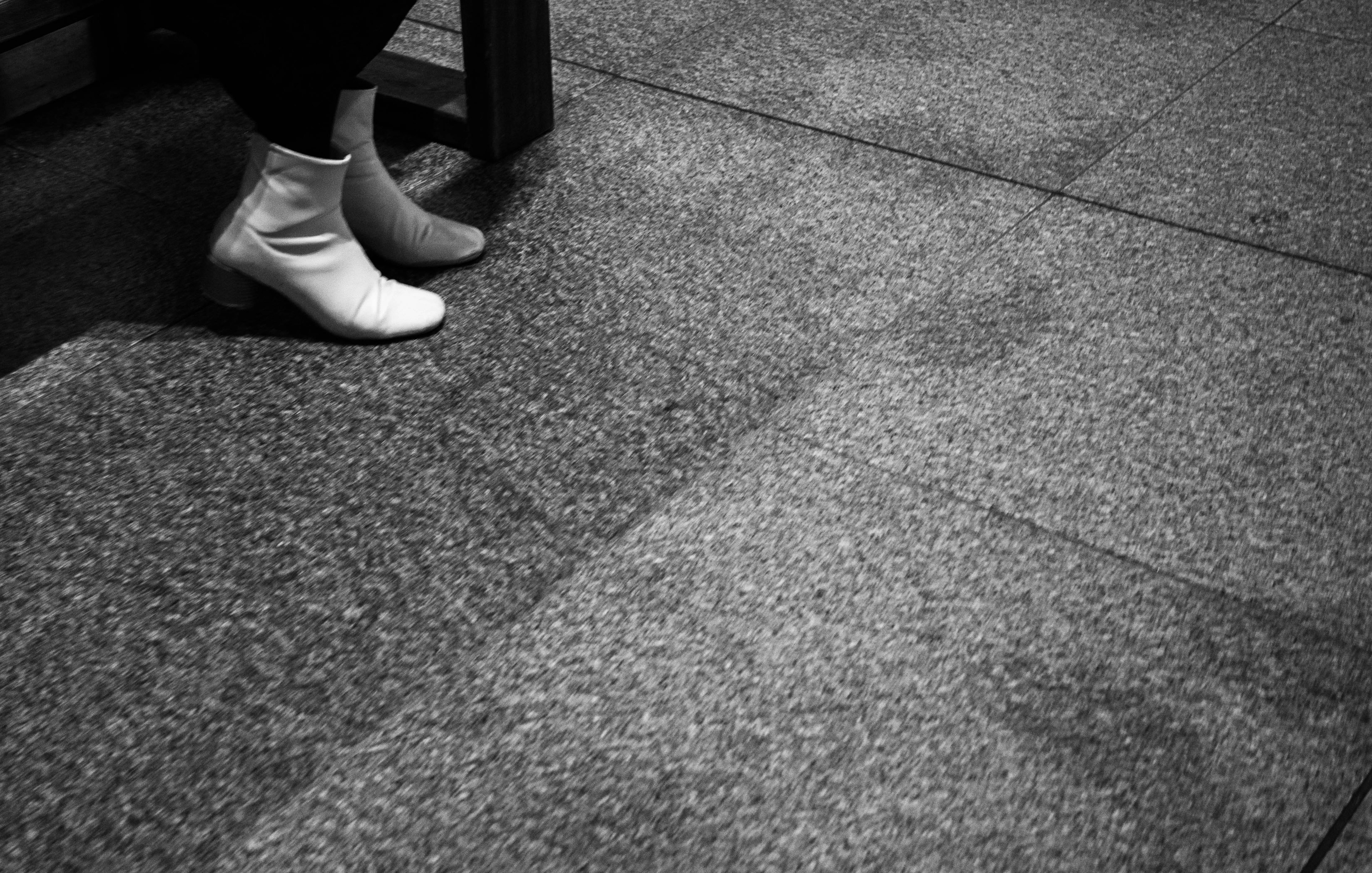 A pair of feet wearing white and black socks resting on a textured floor in black and white