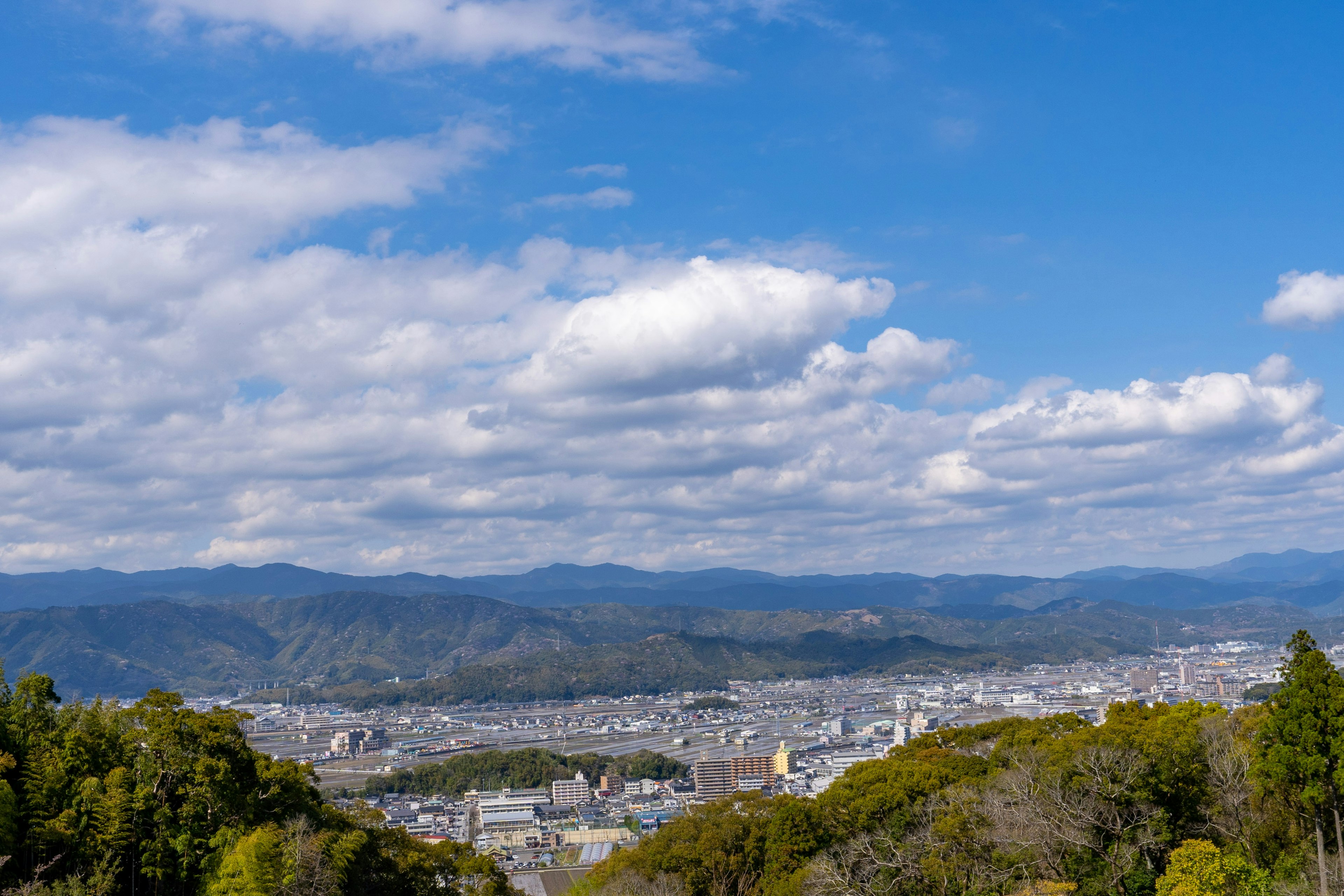 Vista panorámica de una vasta ciudad con montañas al fondo bajo un cielo azul y nubes