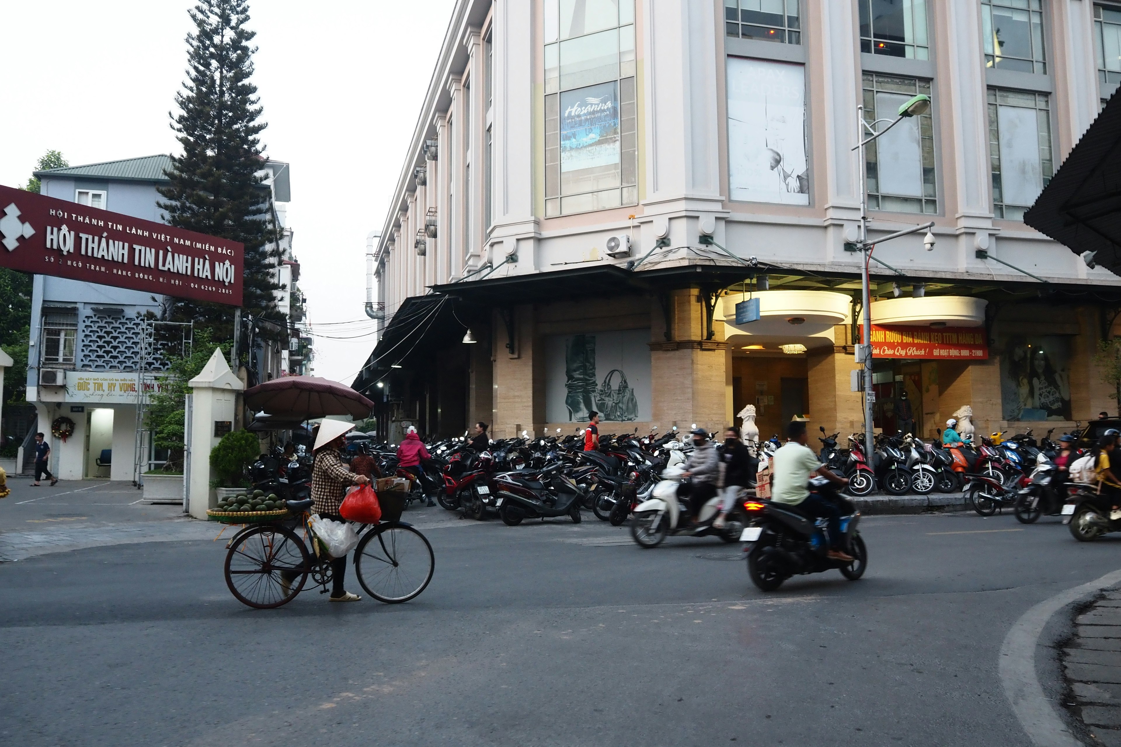 Busy intersection with motorcycles and bicycles Commercial building in the background Many parked bikes