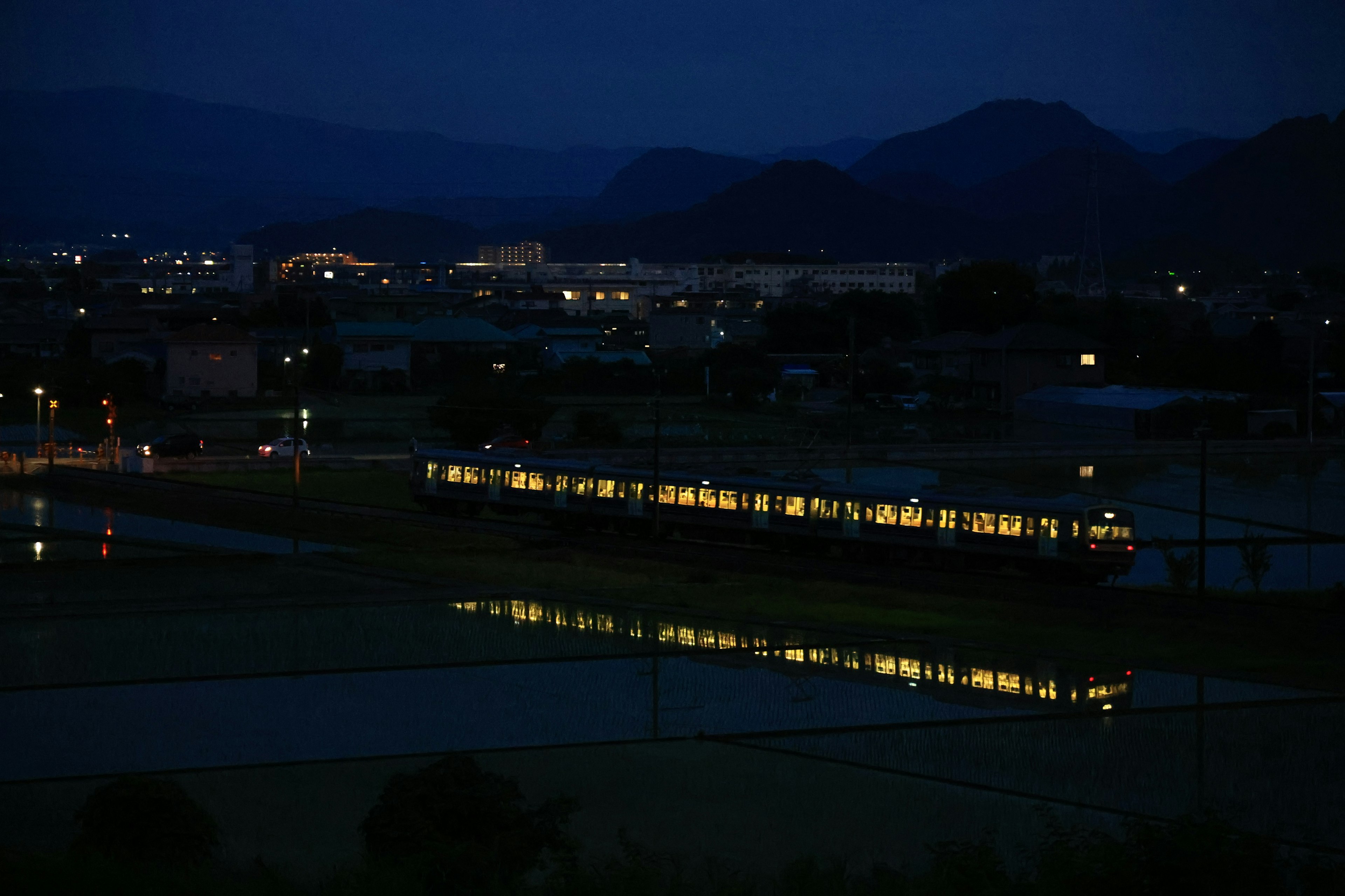 Train illuminated at night reflecting in water with mountains in the background