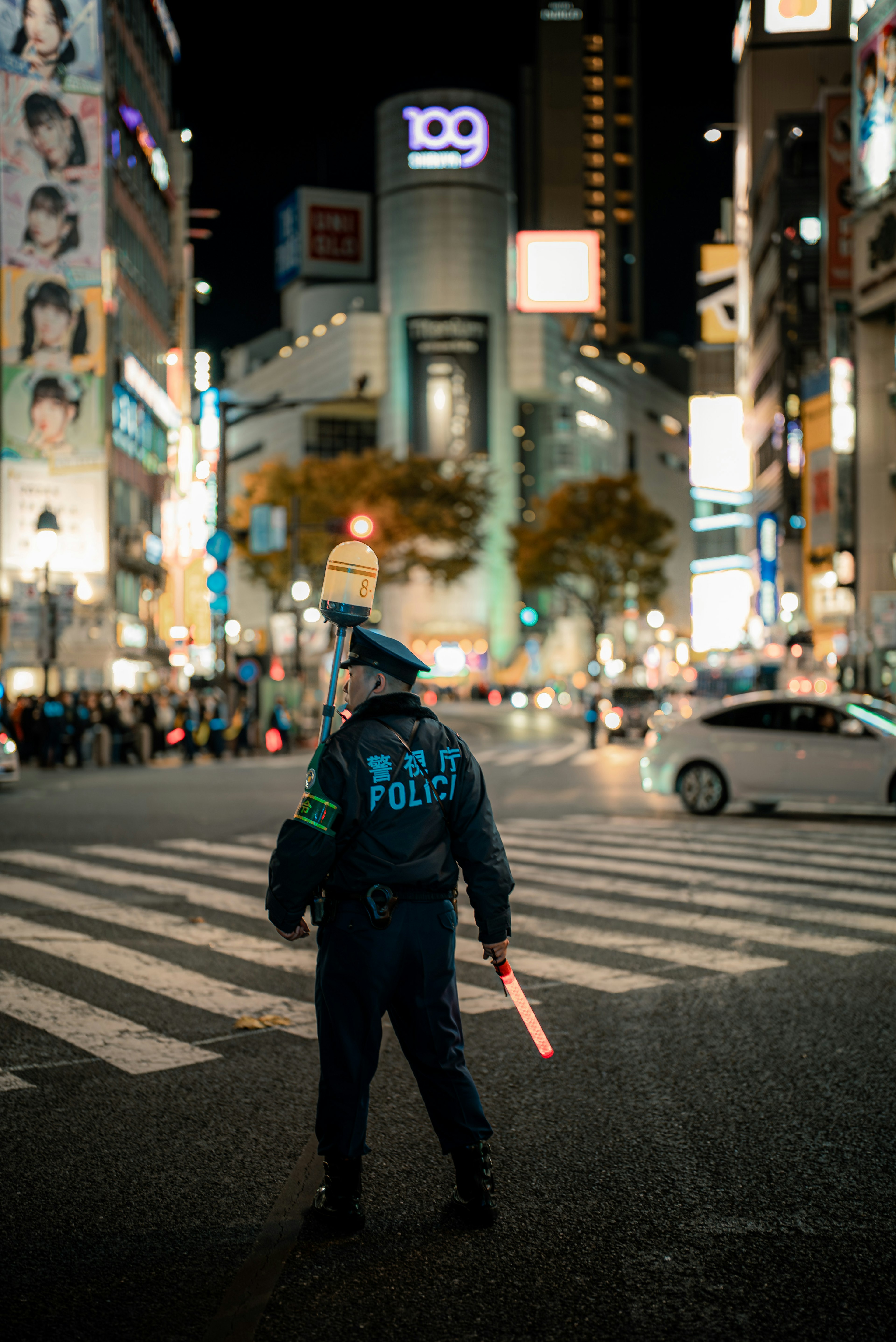 Seorang polisi berdiri dengan lampu merah di jalan-jalan ramai Shibuya di malam hari