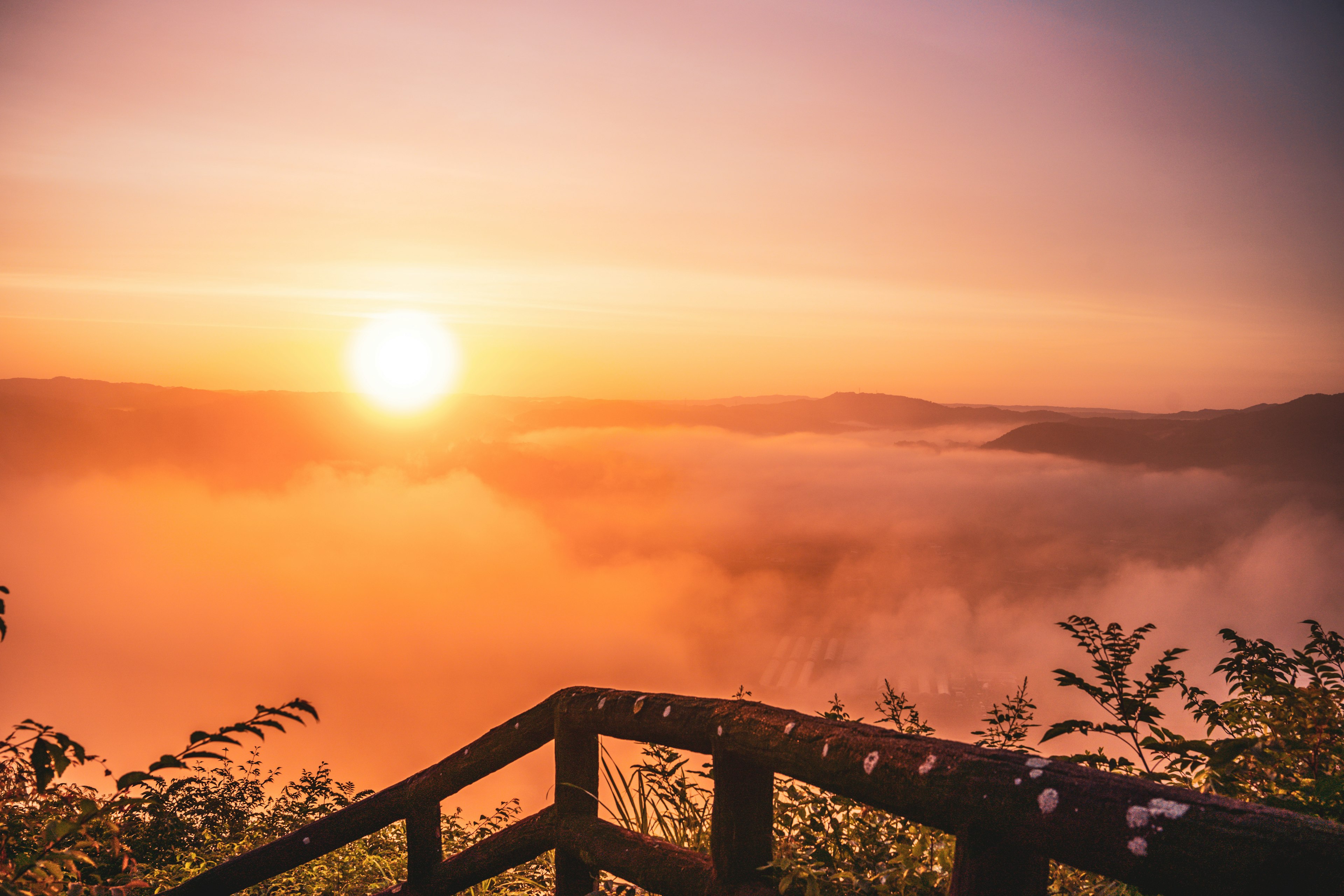 Beautiful sunrise above fog with wooden railing in view