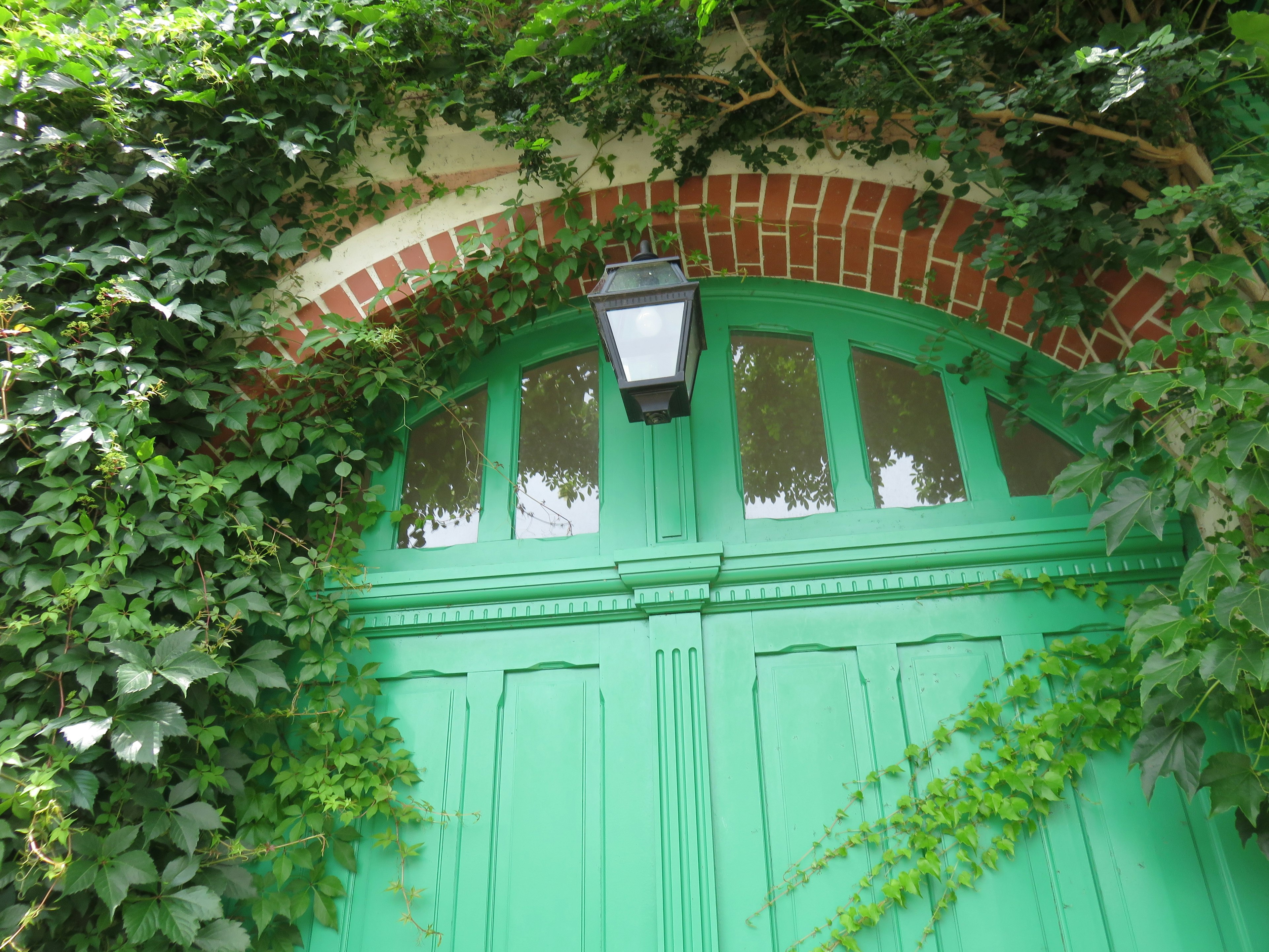 Green door framed by a brick arch with a lantern and ivy plants