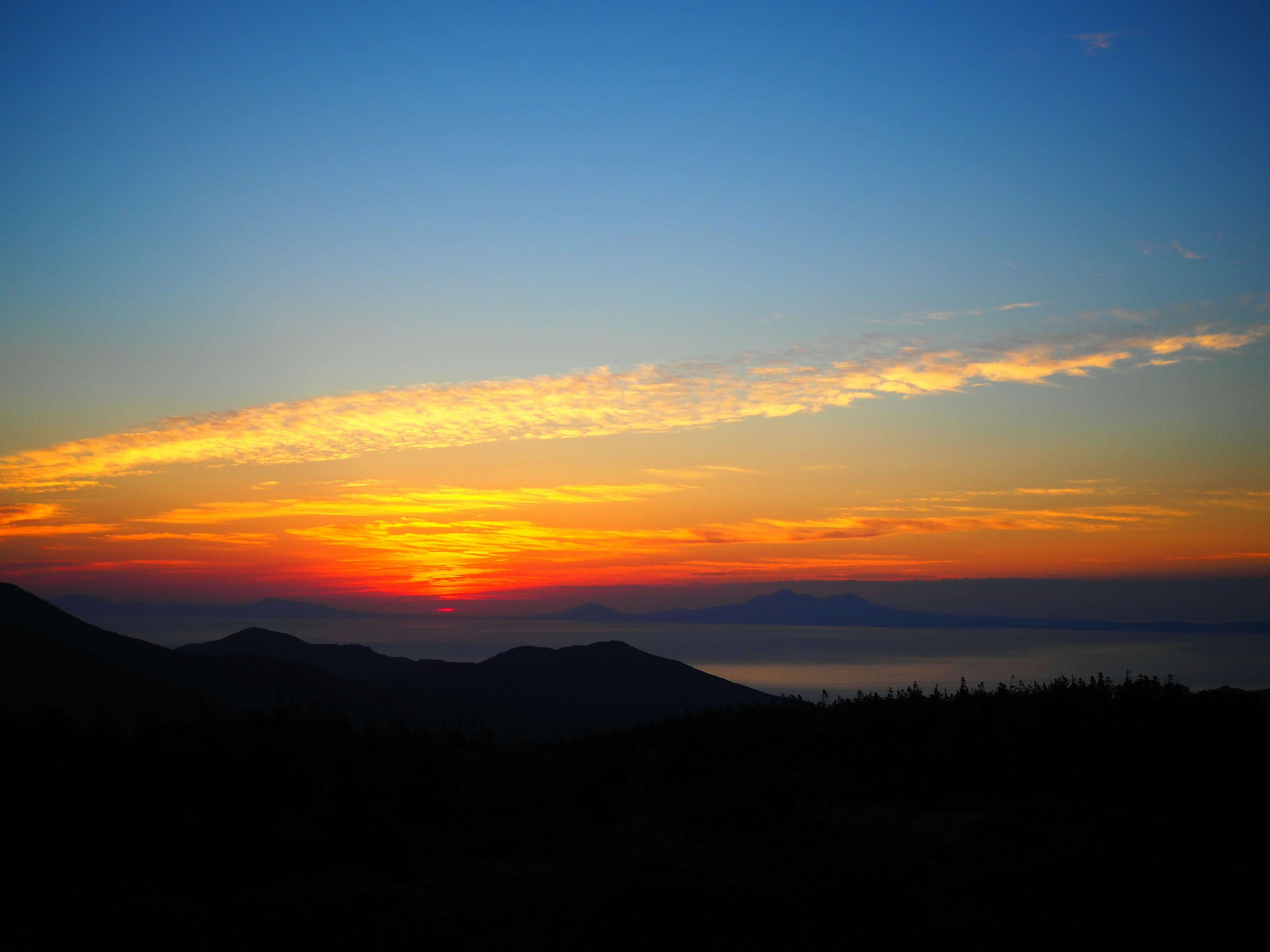 Bellissimo paesaggio al tramonto con sfumature di arancione e blu montagne in silhouette