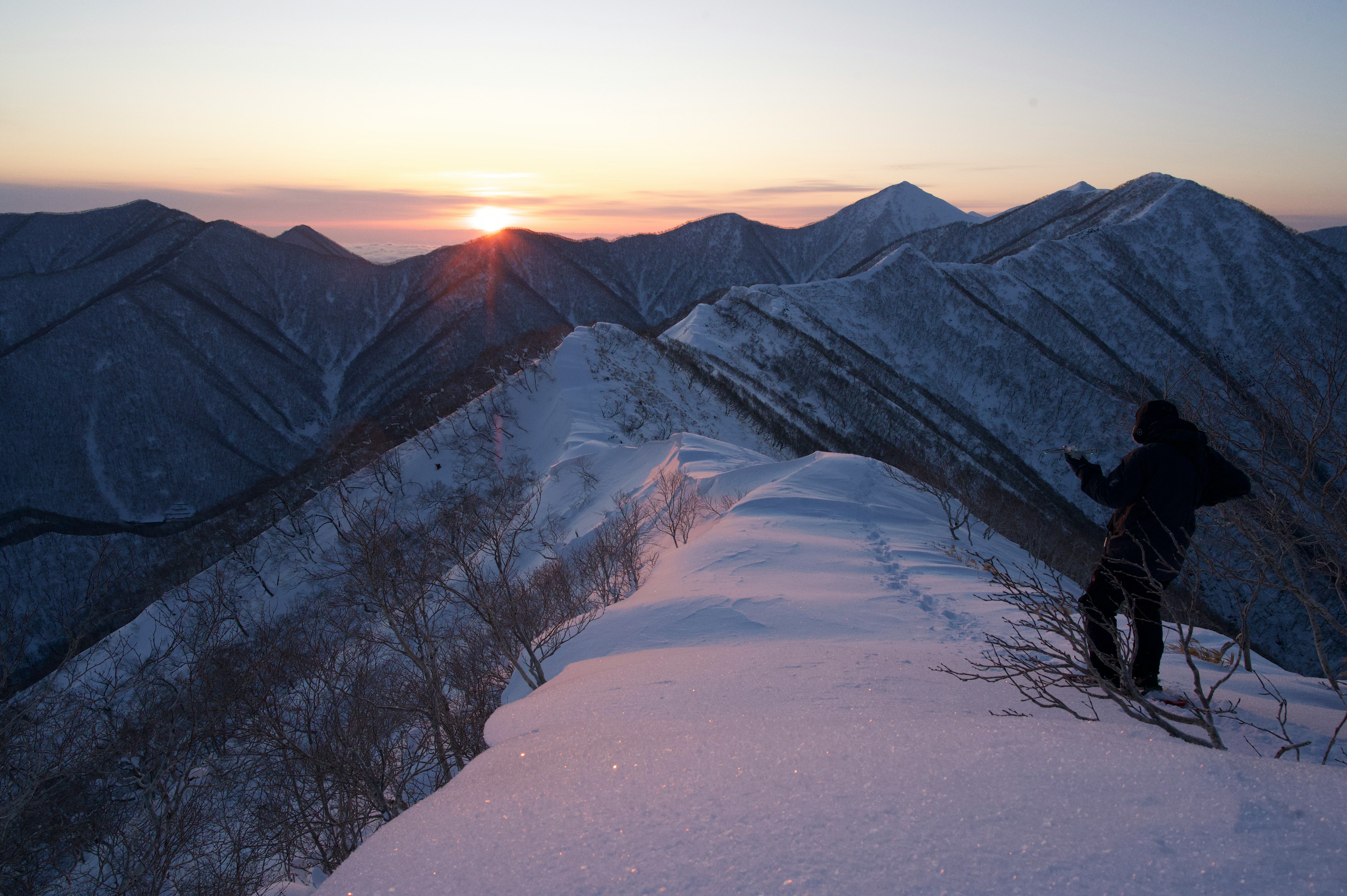 Person standing on snowy mountain ridge watching sunset