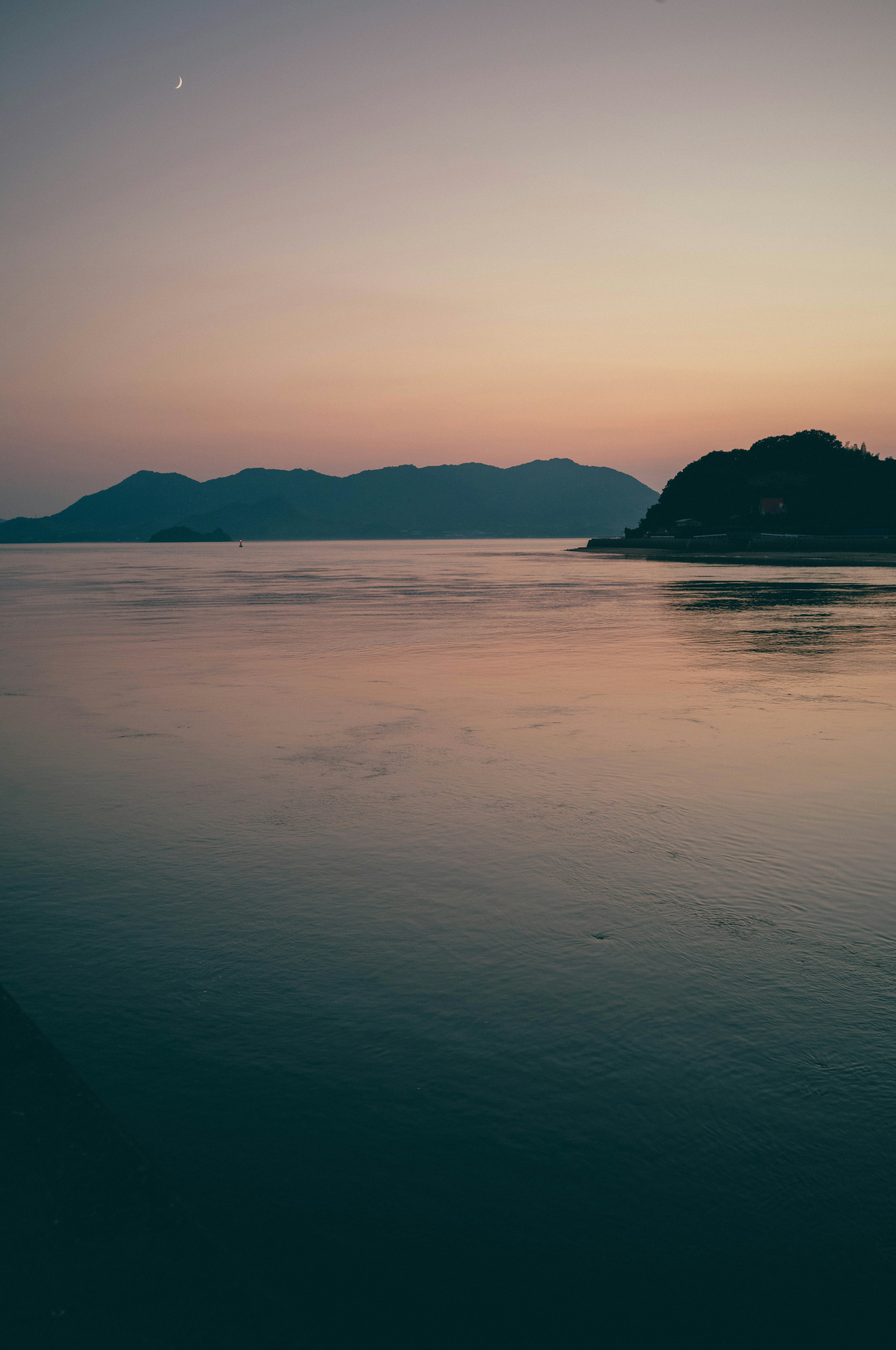 穏やかな水面と山々のシルエットが見える夕焼けの風景