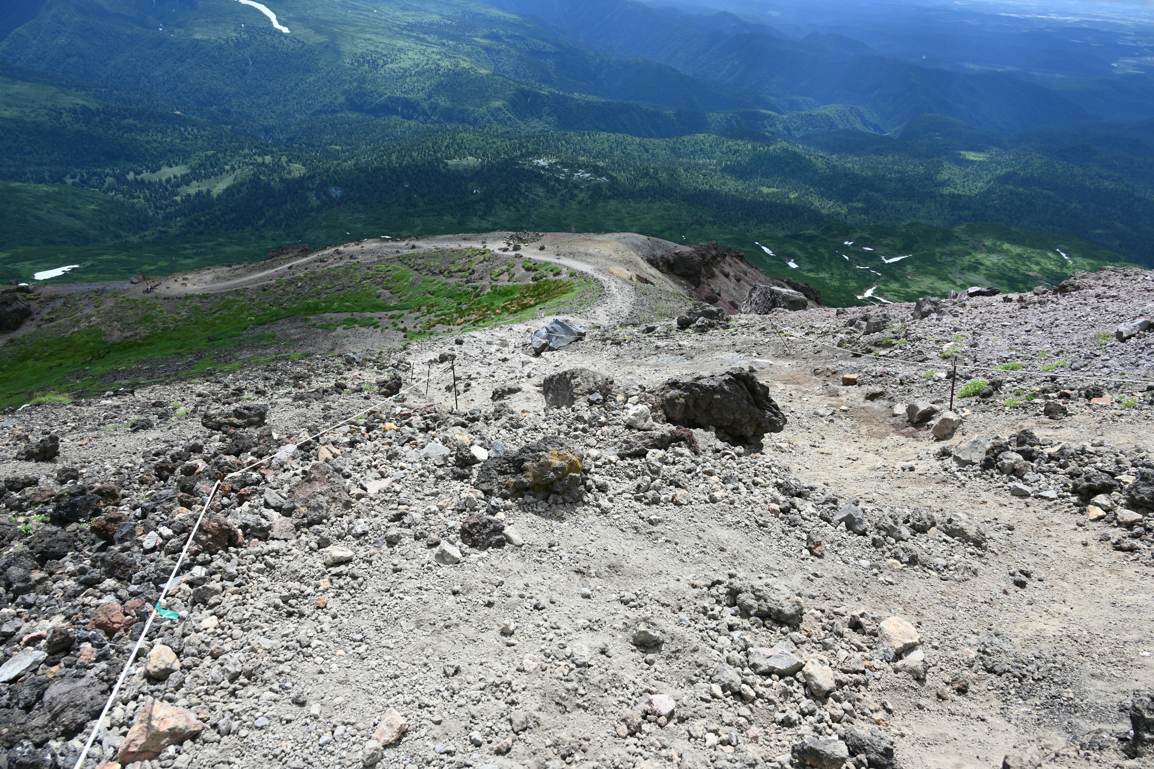 Pemandangan dari puncak gunung menunjukkan jalan berbatu dan vegetasi subur di bawahnya