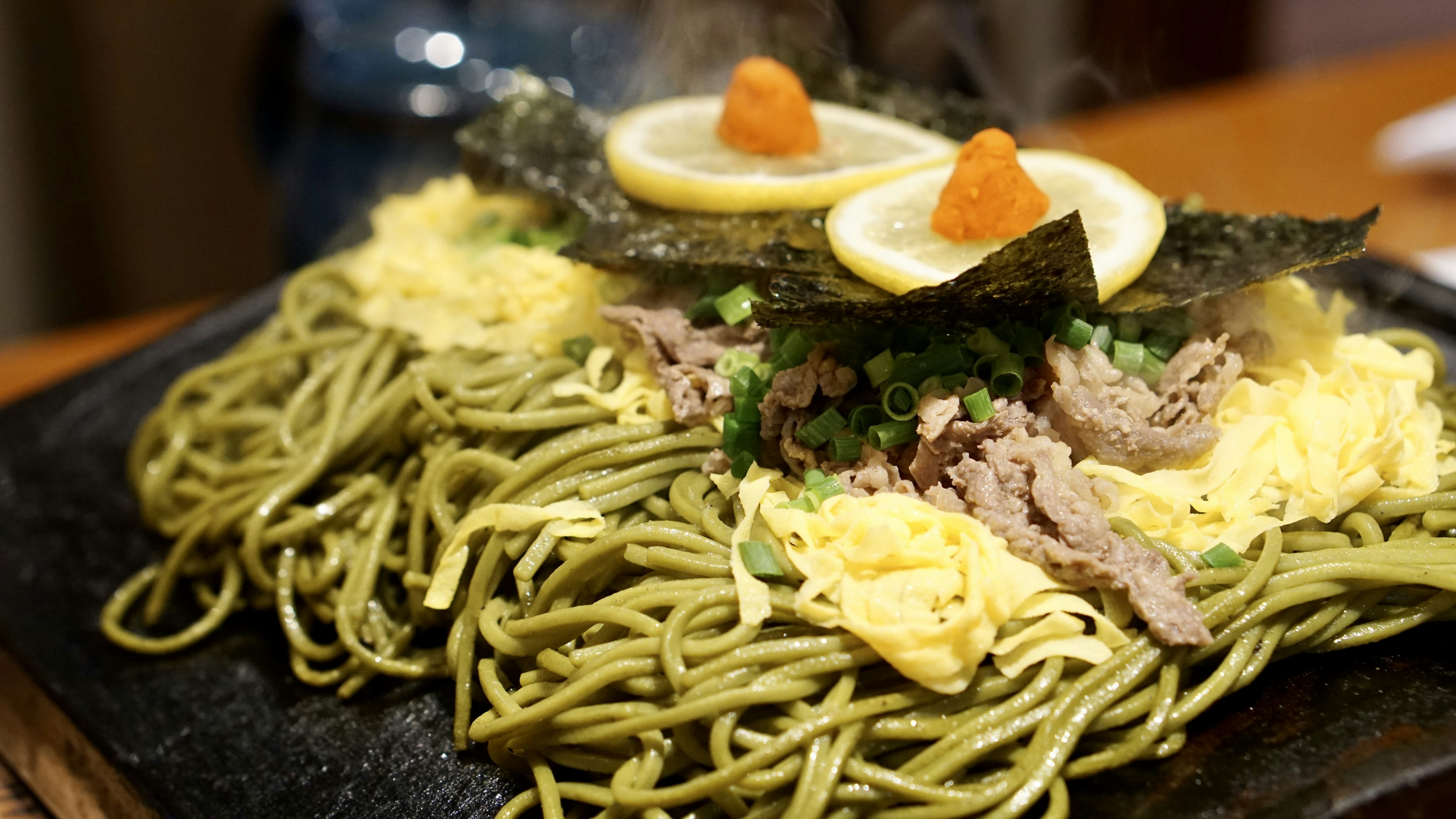 Fideos verdes cubiertos con huevo y algas en un plato humeante