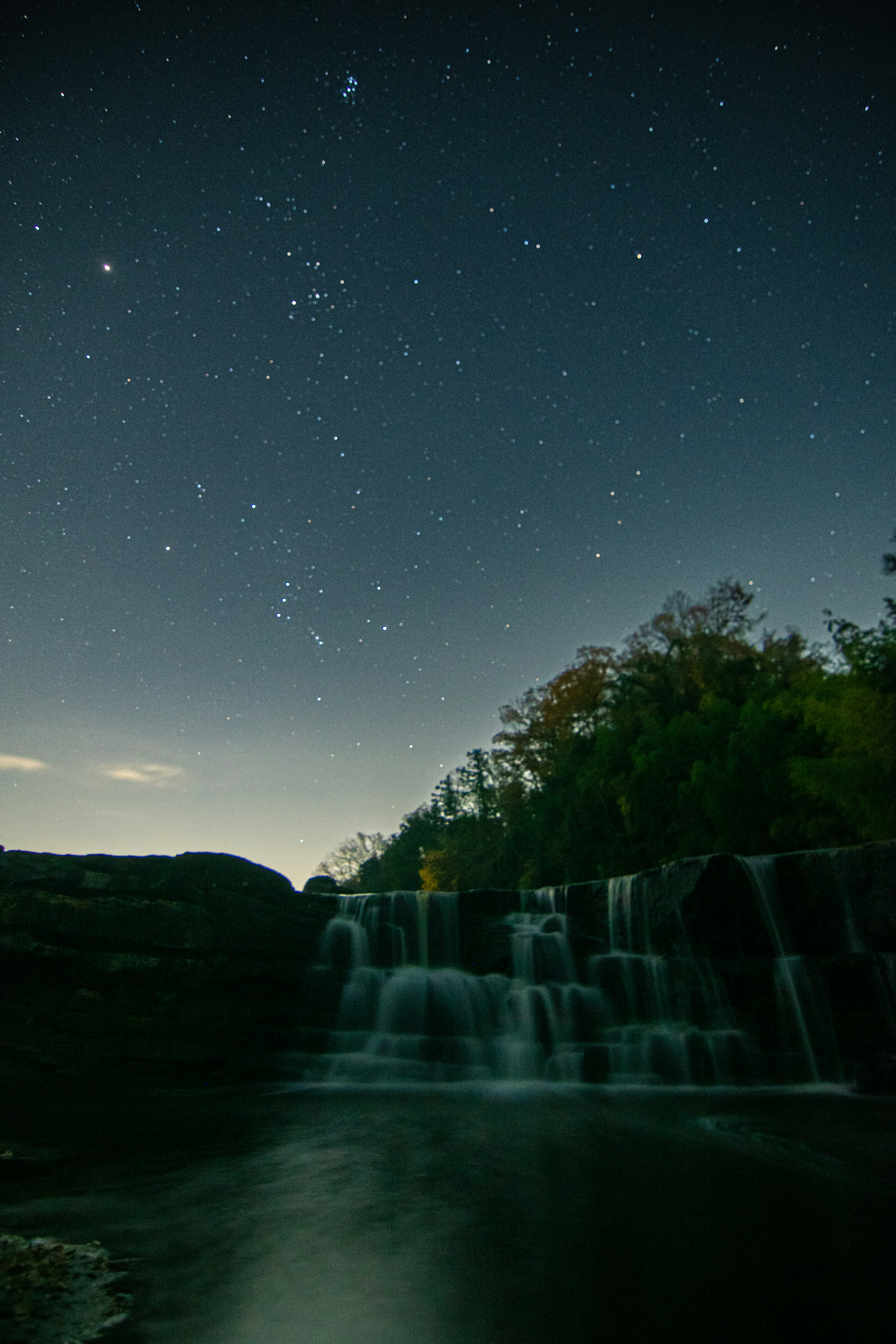 Waterfall flowing under a starry night sky with surrounding trees