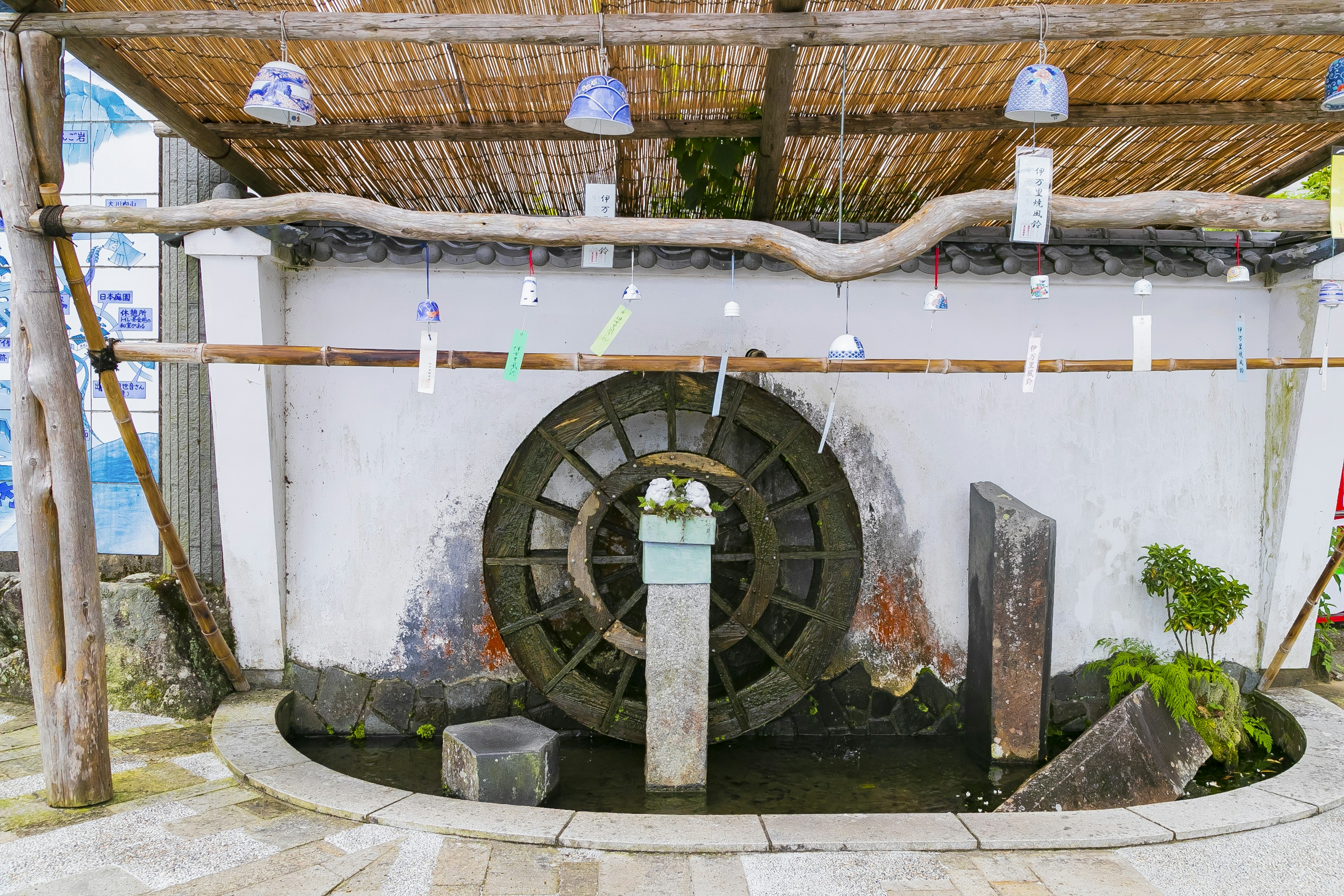 Foto de una rueda de agua con una pared blanca bajo un techo de bambú