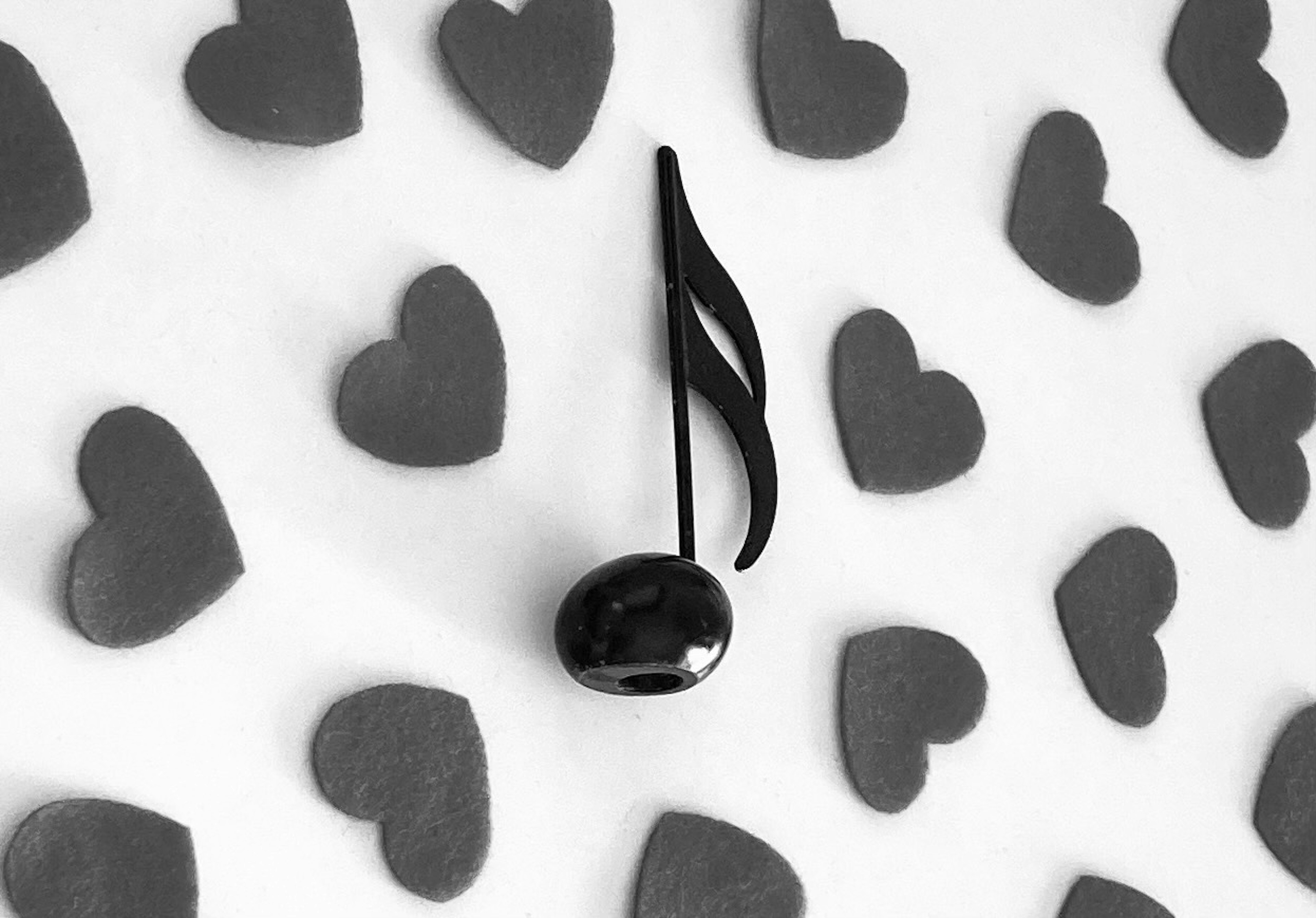 A black musical note on a background of heart shapes in grayscale