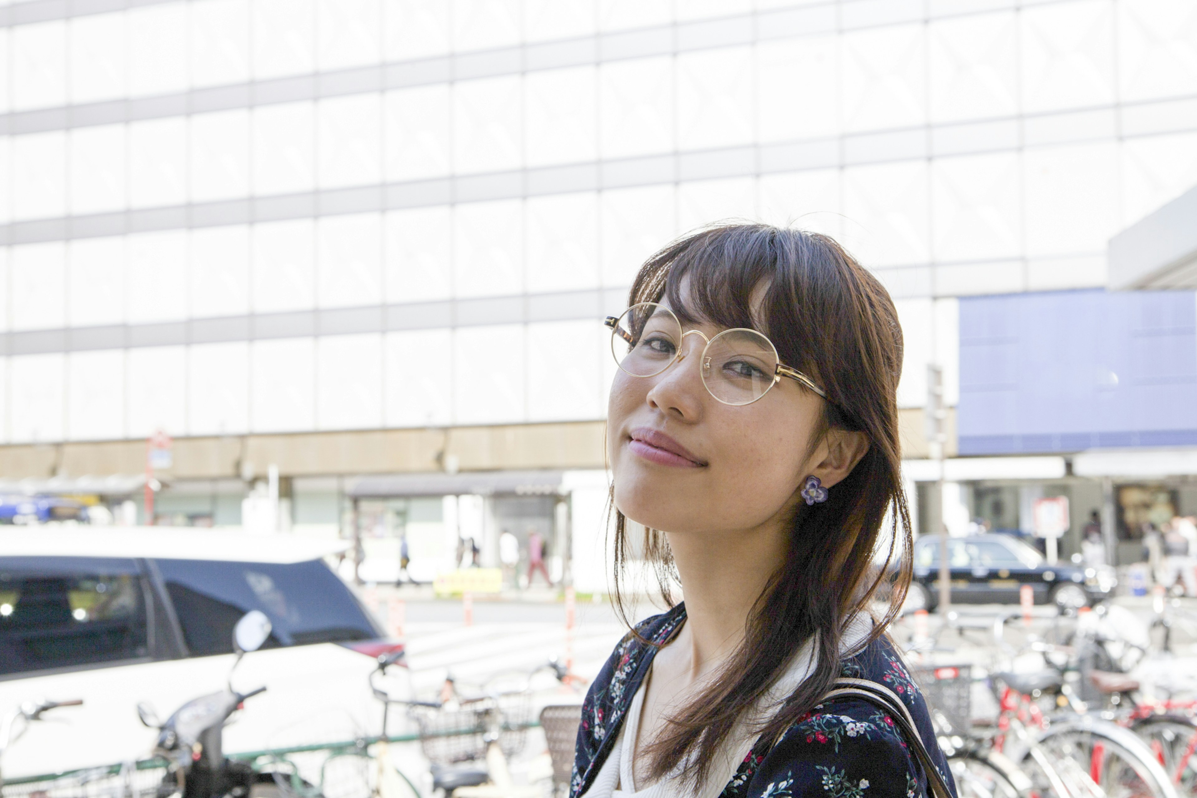 Jeune femme portant des lunettes souriant avec des vélos et un bâtiment en arrière-plan