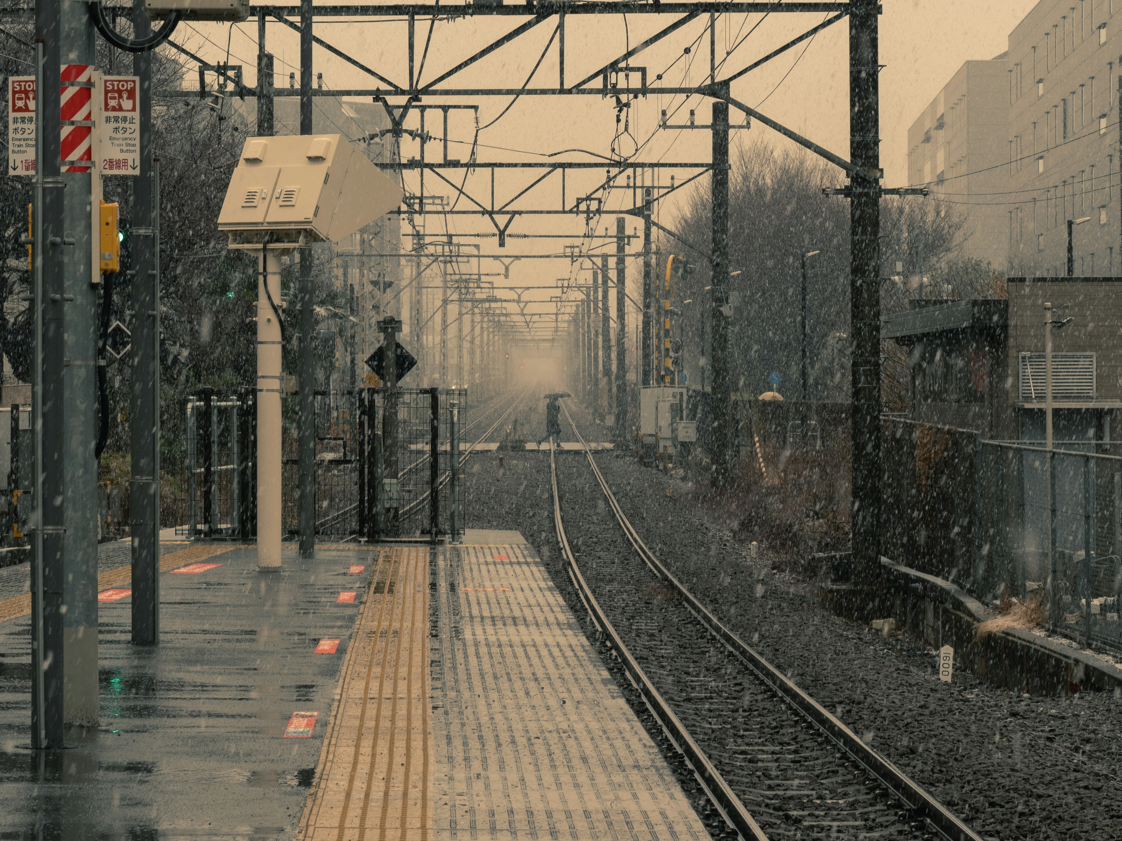 Snowy train station platform with visible tracks and overhead wires