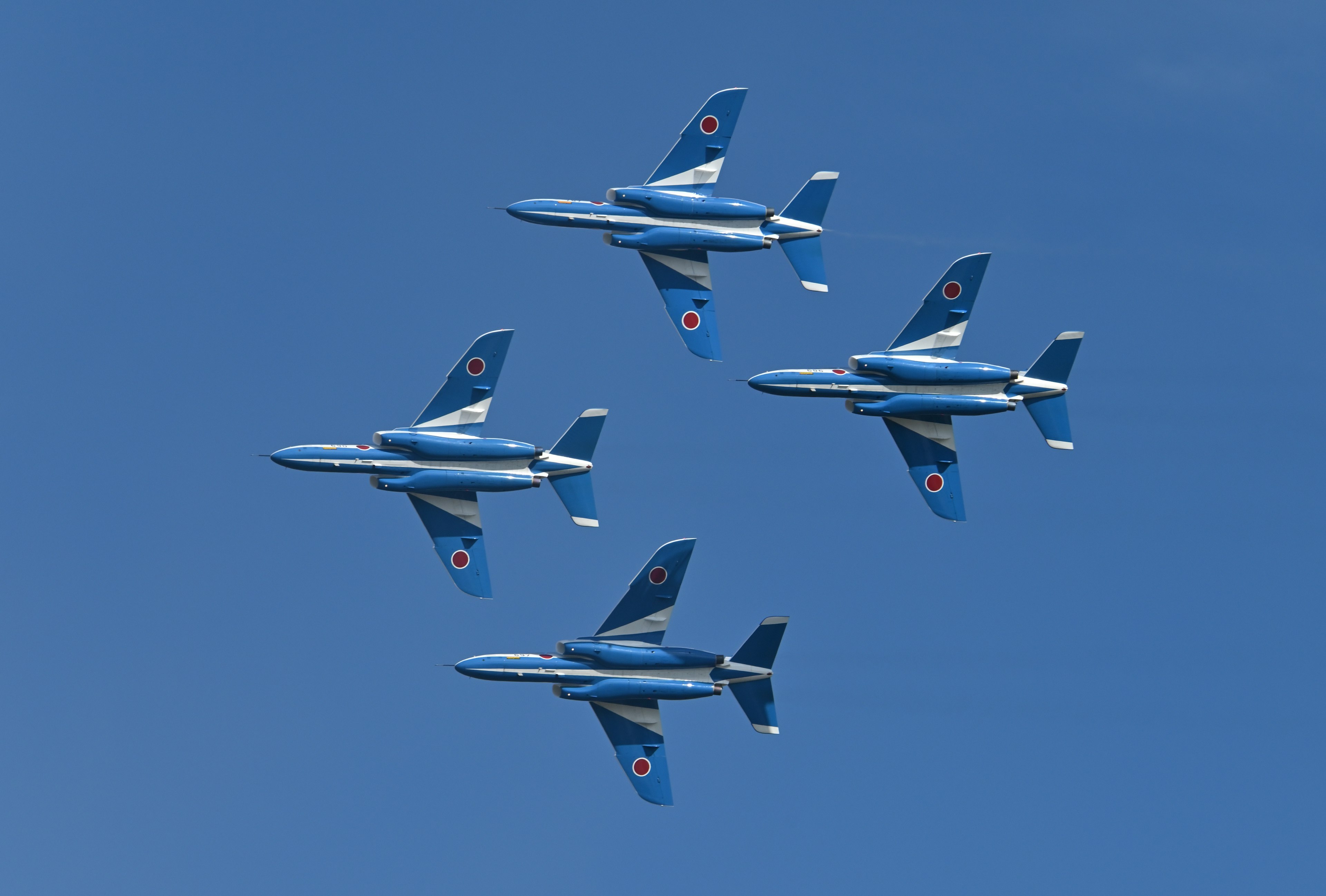 Vier blaue Kampfjets fliegen in einem klaren blauen Himmel