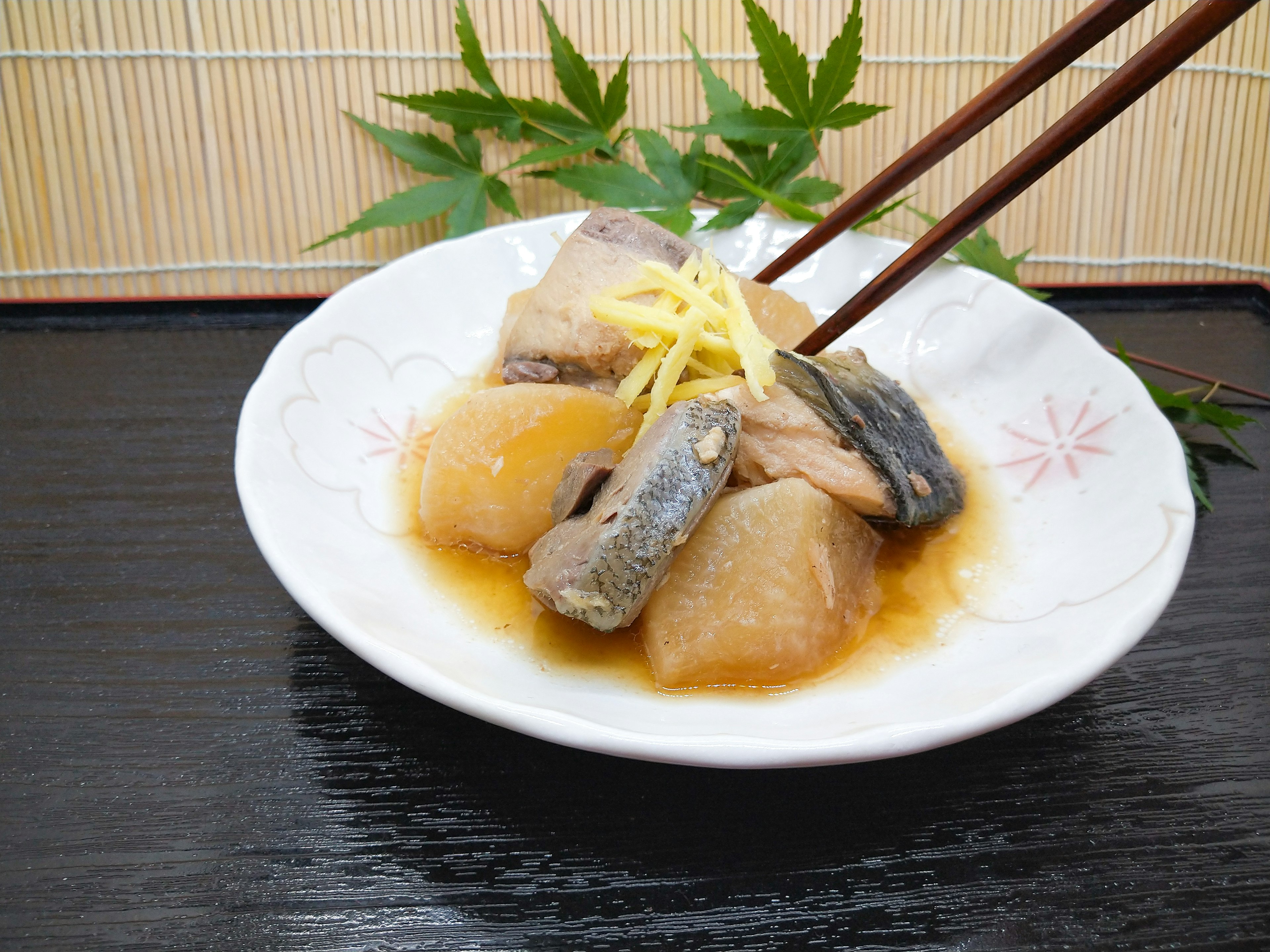 Un piatto bianco con pesce giapponese in umido e daikon guarnito con zenzero