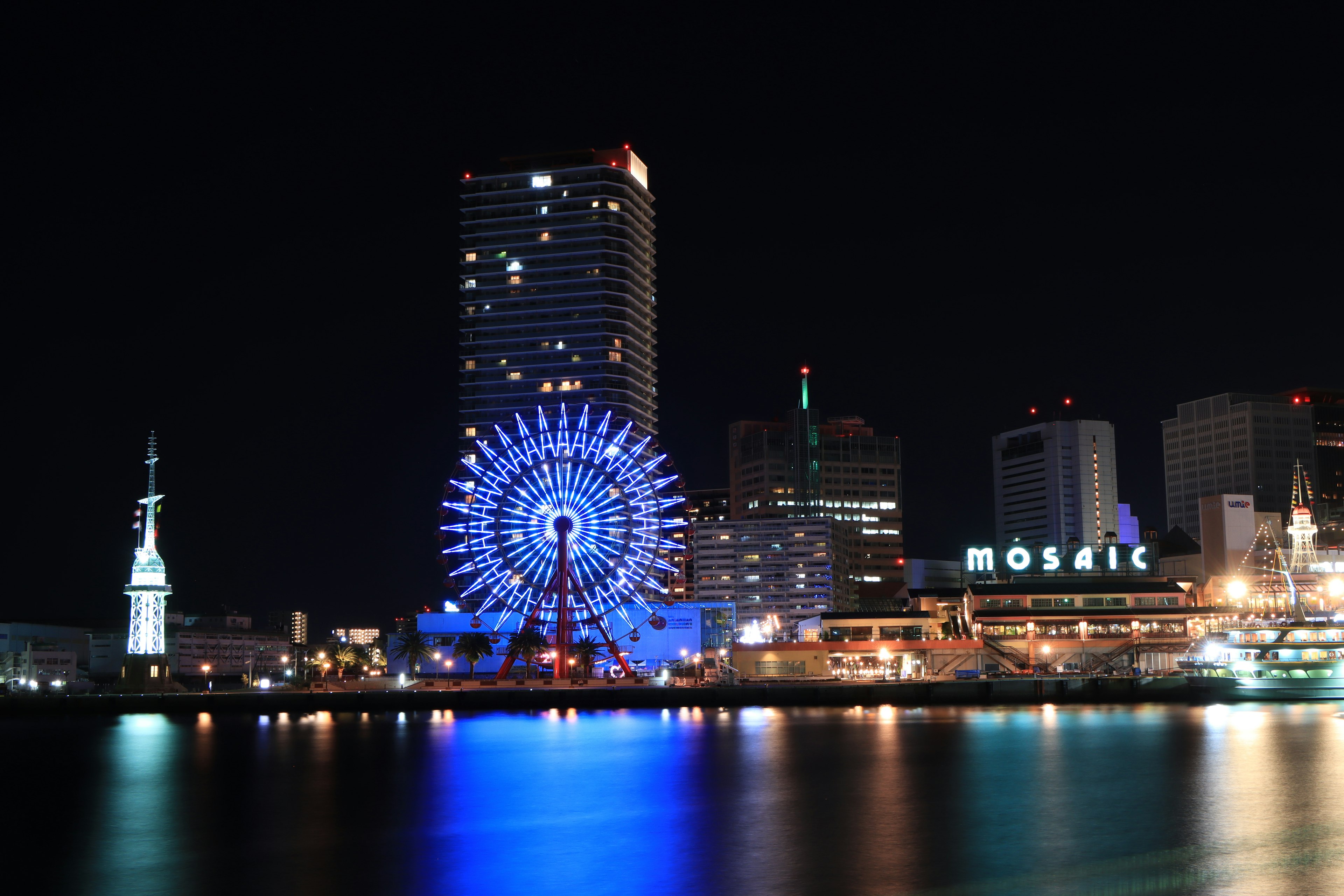 Night view of a waterfront featuring a ferris wheel and skyscrapers with a Mosaic sign