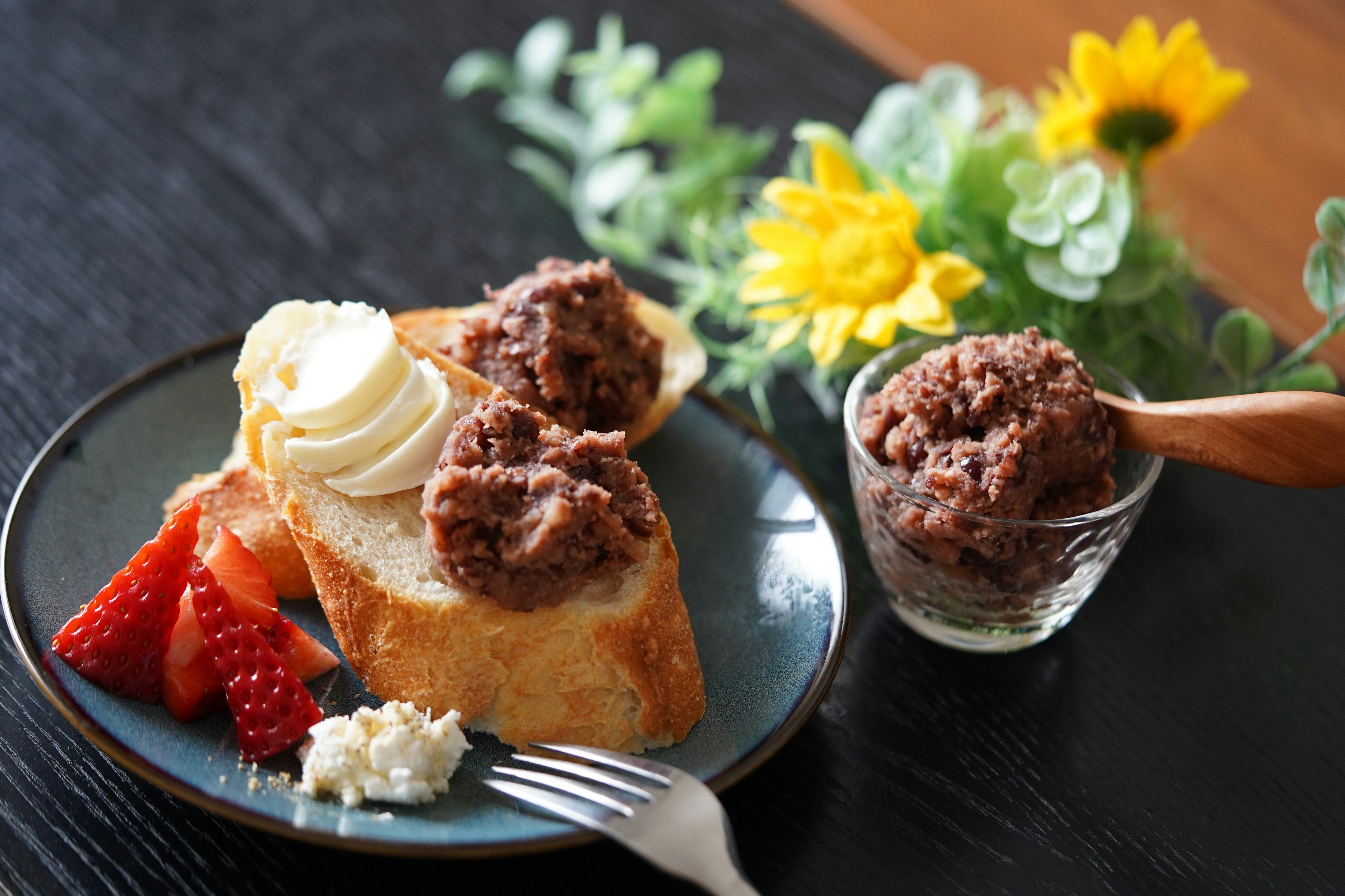 Une assiette avec du pain garni de crème et de pâte de haricots rouges accompagnée de fraises et de fleurs