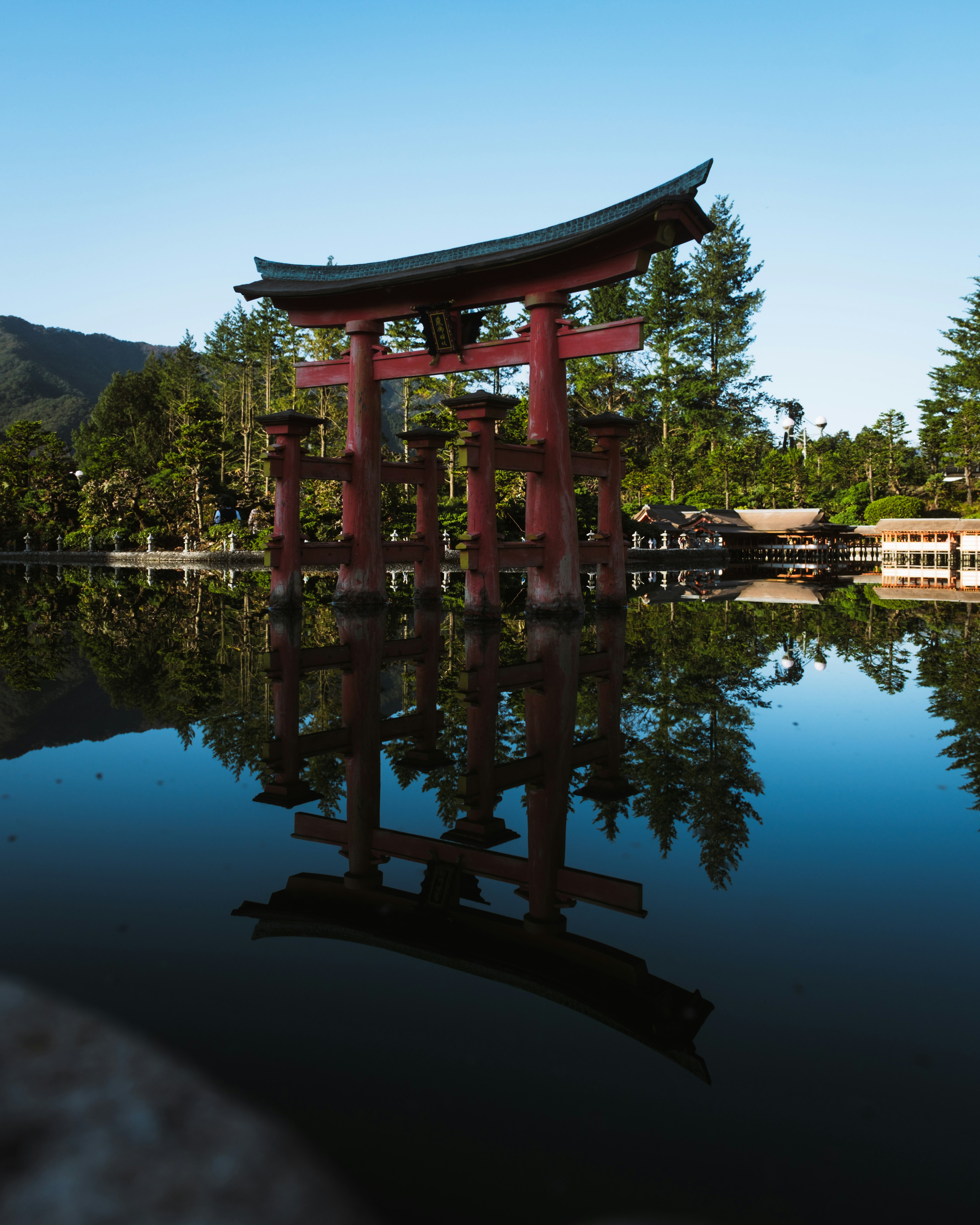 Red torii gate reflecting in a calm lake surrounded by green trees