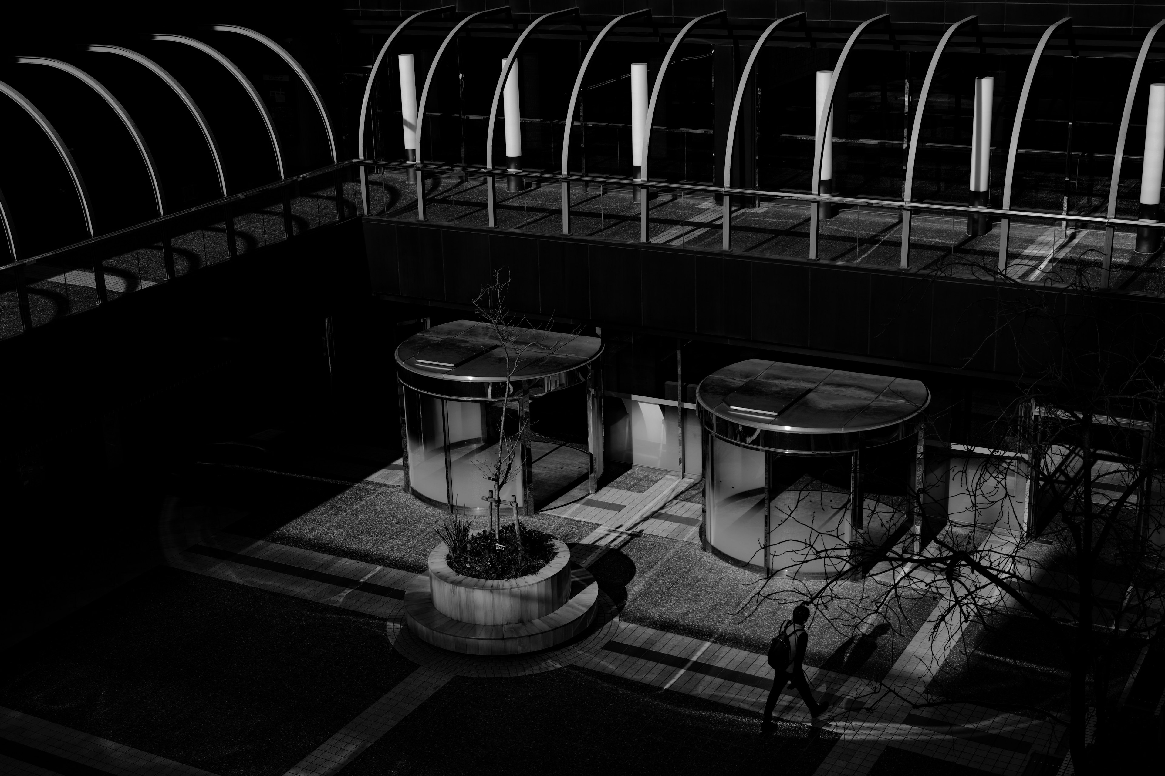 Photo en noir et blanc d'un espace intérieur avec des portes tournantes et une fontaine au centre sous un plafond en verre en arc