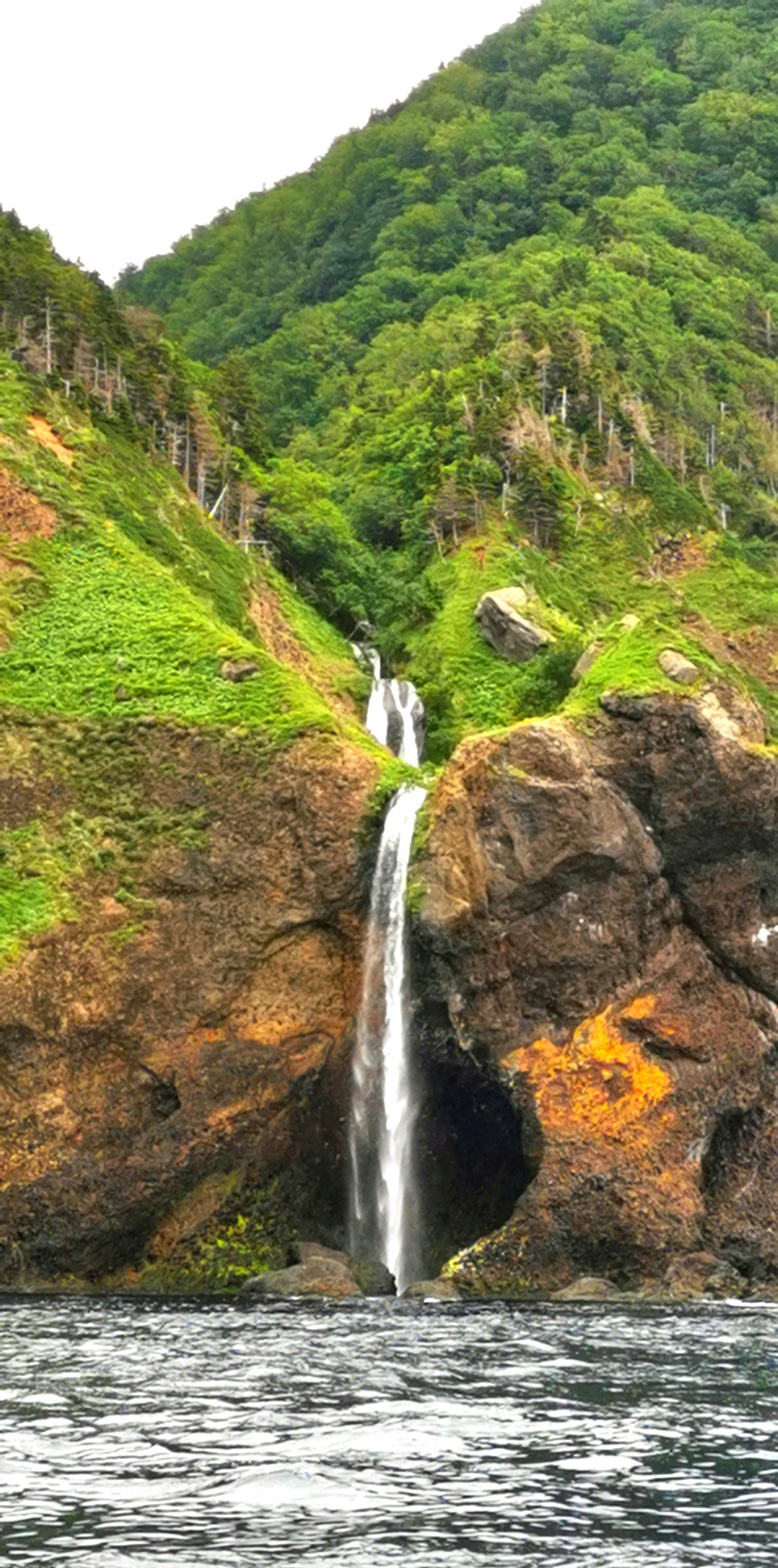 Malerischer Wasserfall, der von felsigen Klippen umgeben von üppigen grünen Bergen herabstürzt