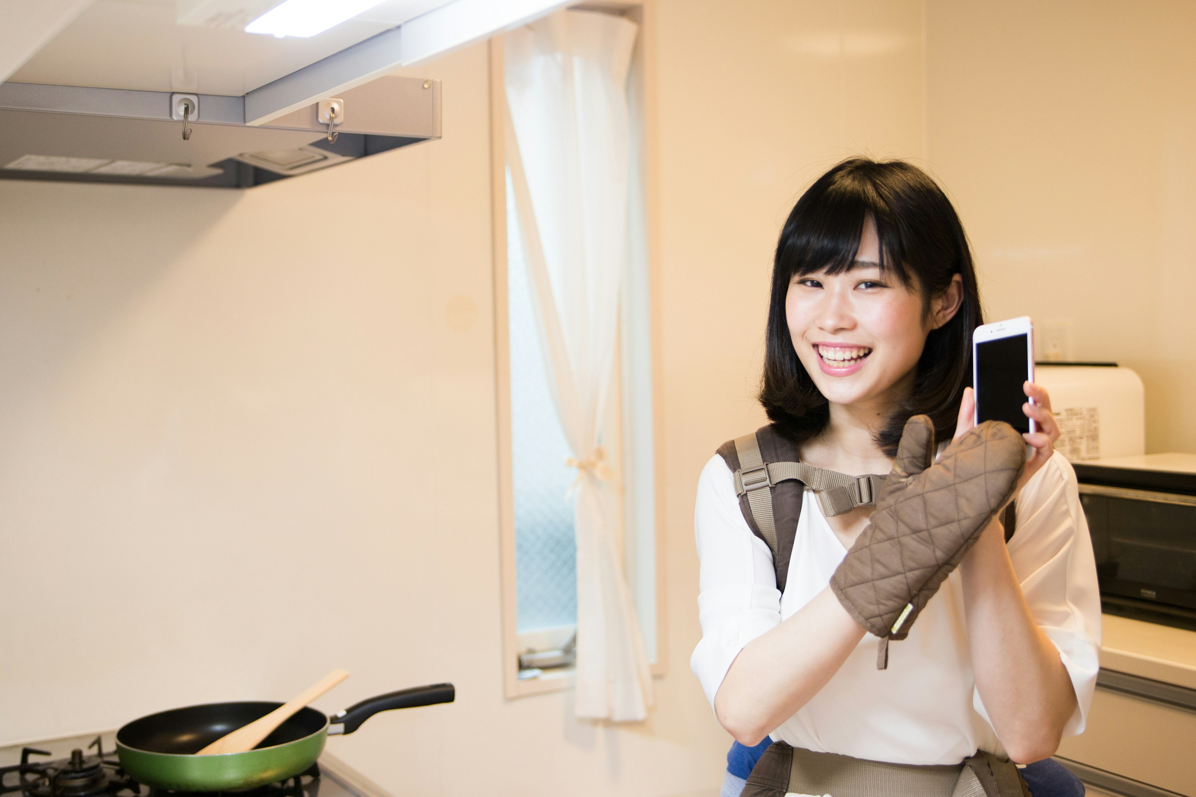 Mujer sonriendo en una cocina sosteniendo un smartphone