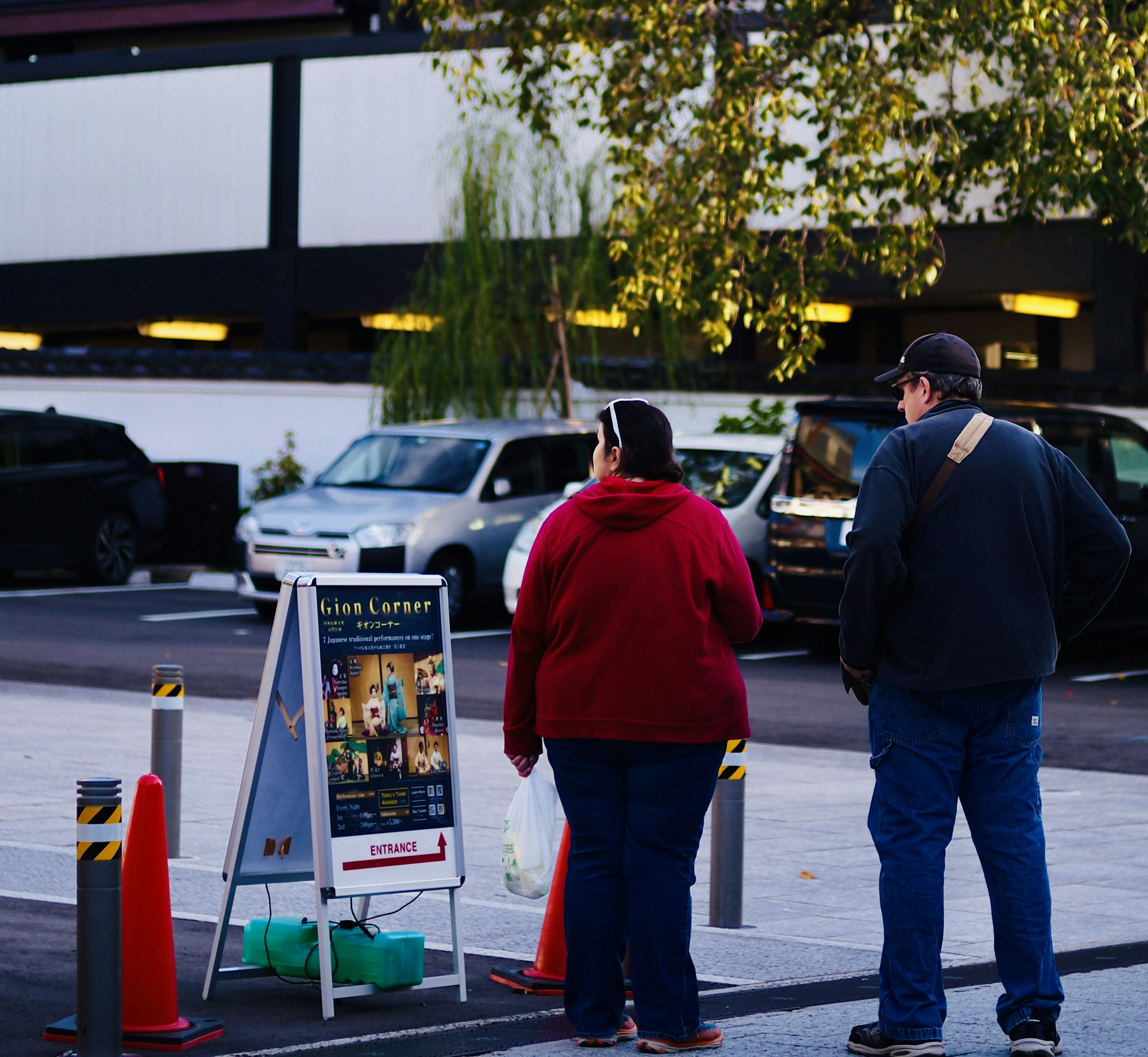 A woman in a red jacket and a man in a gray jacket are looking at a sign in a parking lot