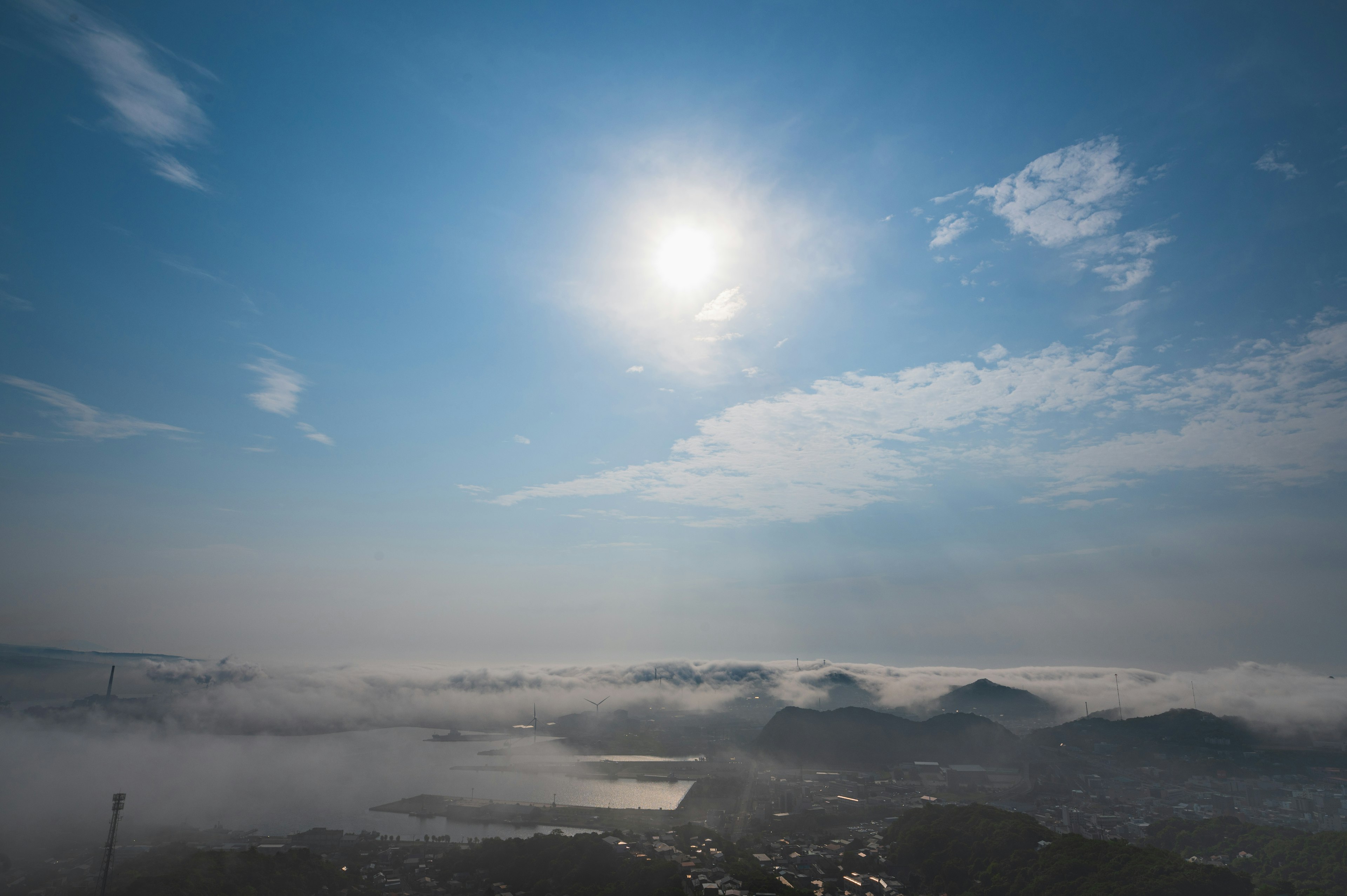 青空に太陽が輝く風景と霧に包まれた山々