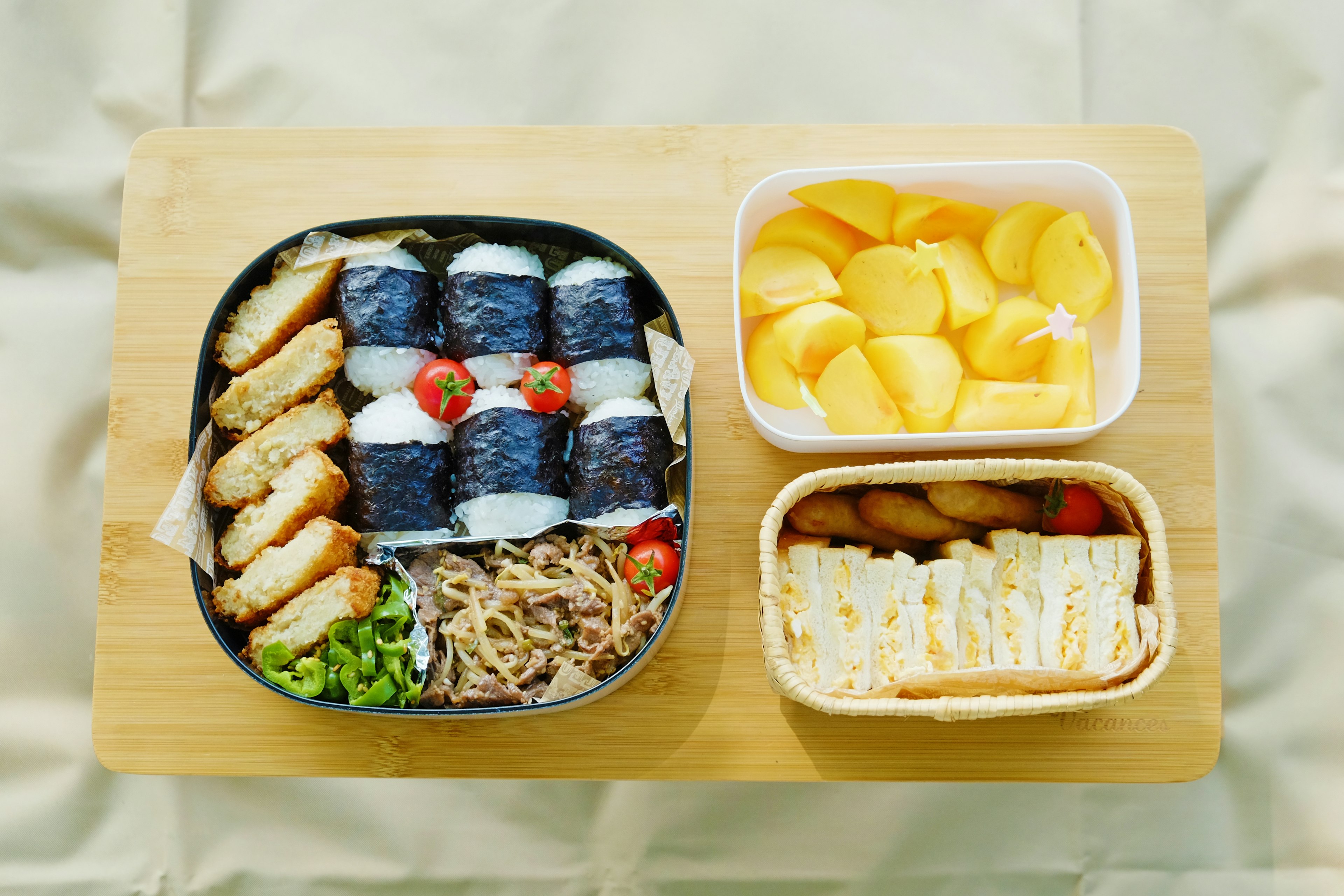 Bento box featuring sushi rolls fried items bean sprouts green vegetables and sliced fruit