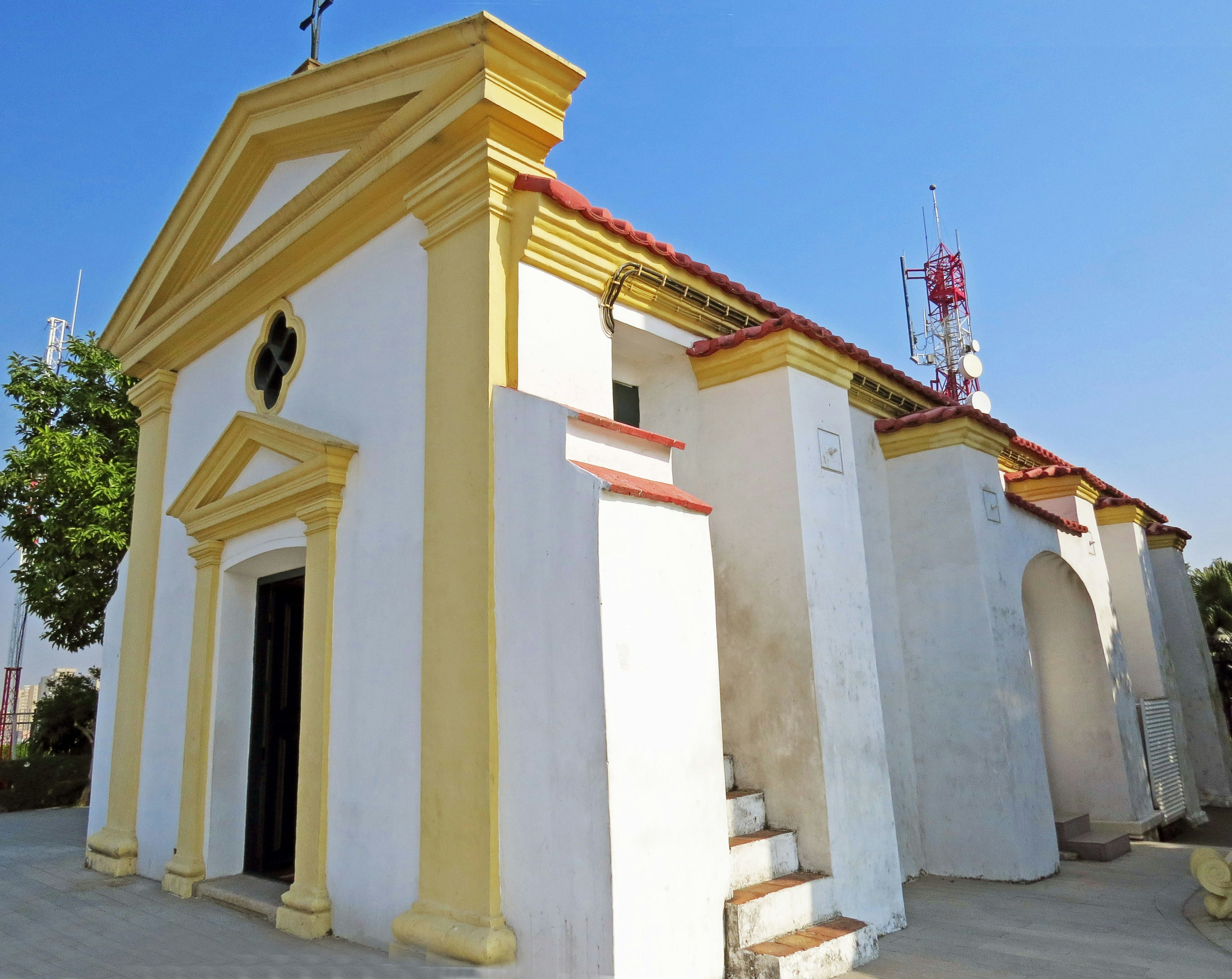 Eksterior gereja putih dengan aksen kuning di bawah langit biru yang cerah