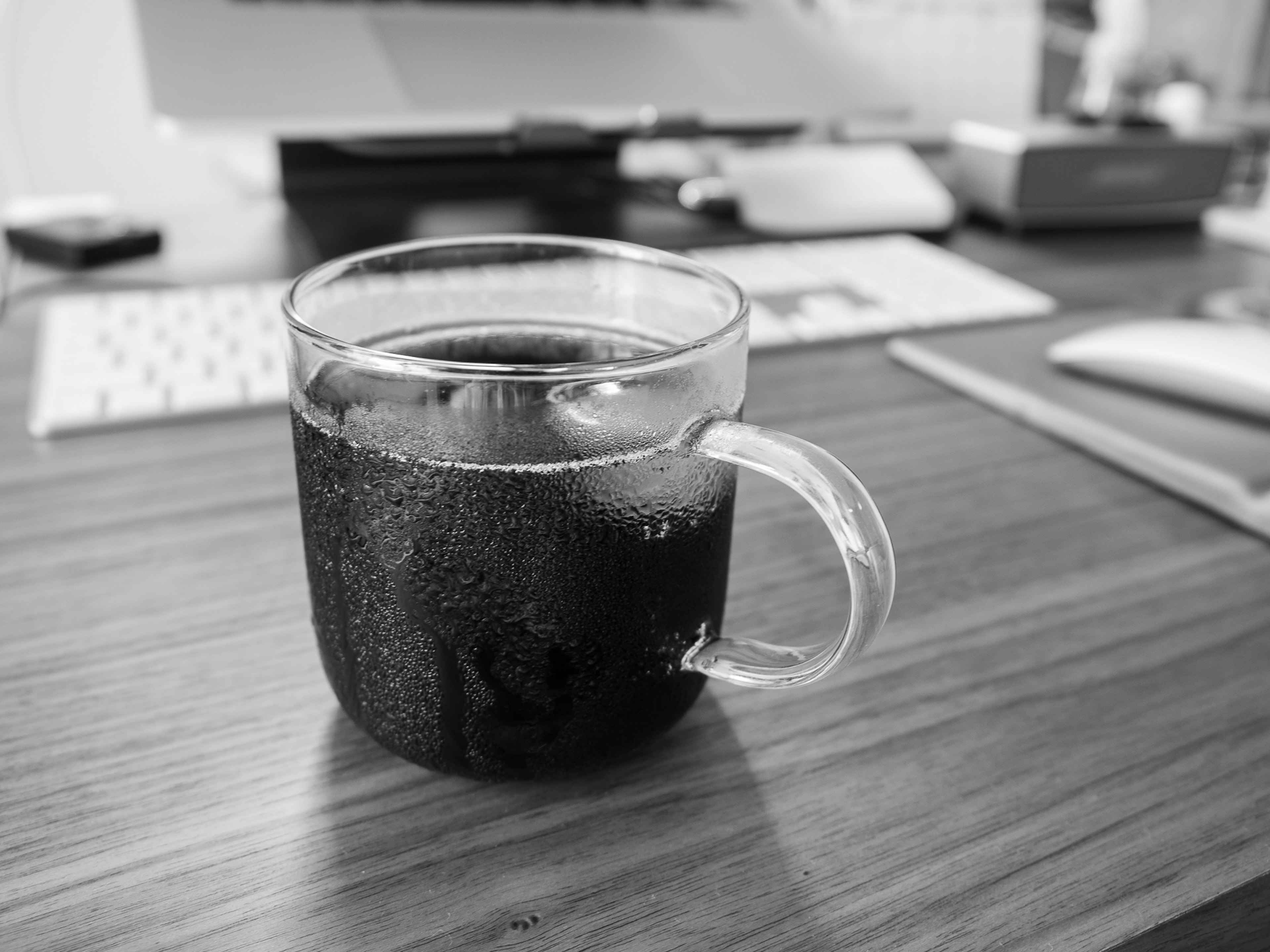 Une tasse en verre transparent remplie de café noir posée sur une table en bois