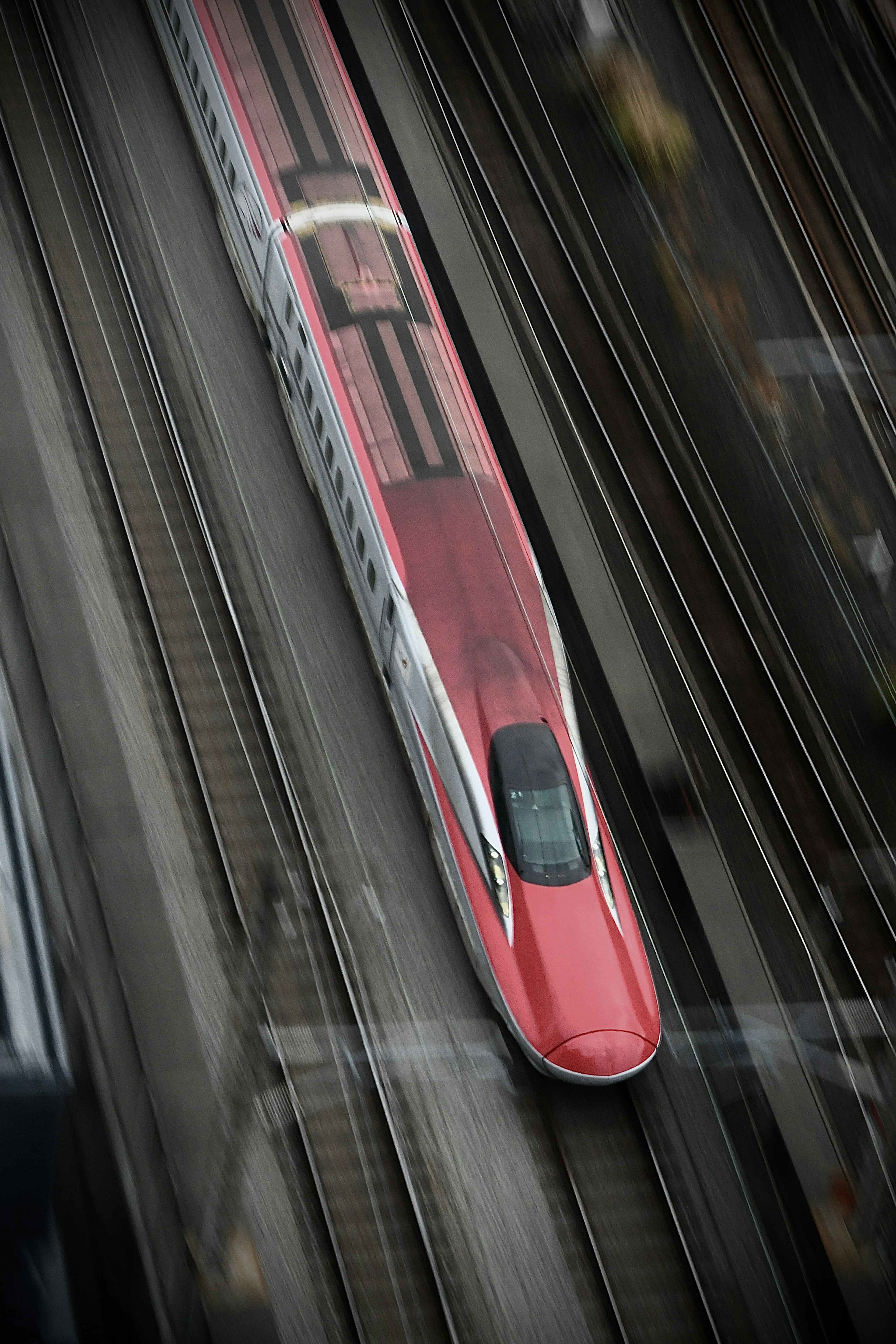 A red Shinkansen train traveling on tracks from an aerial view