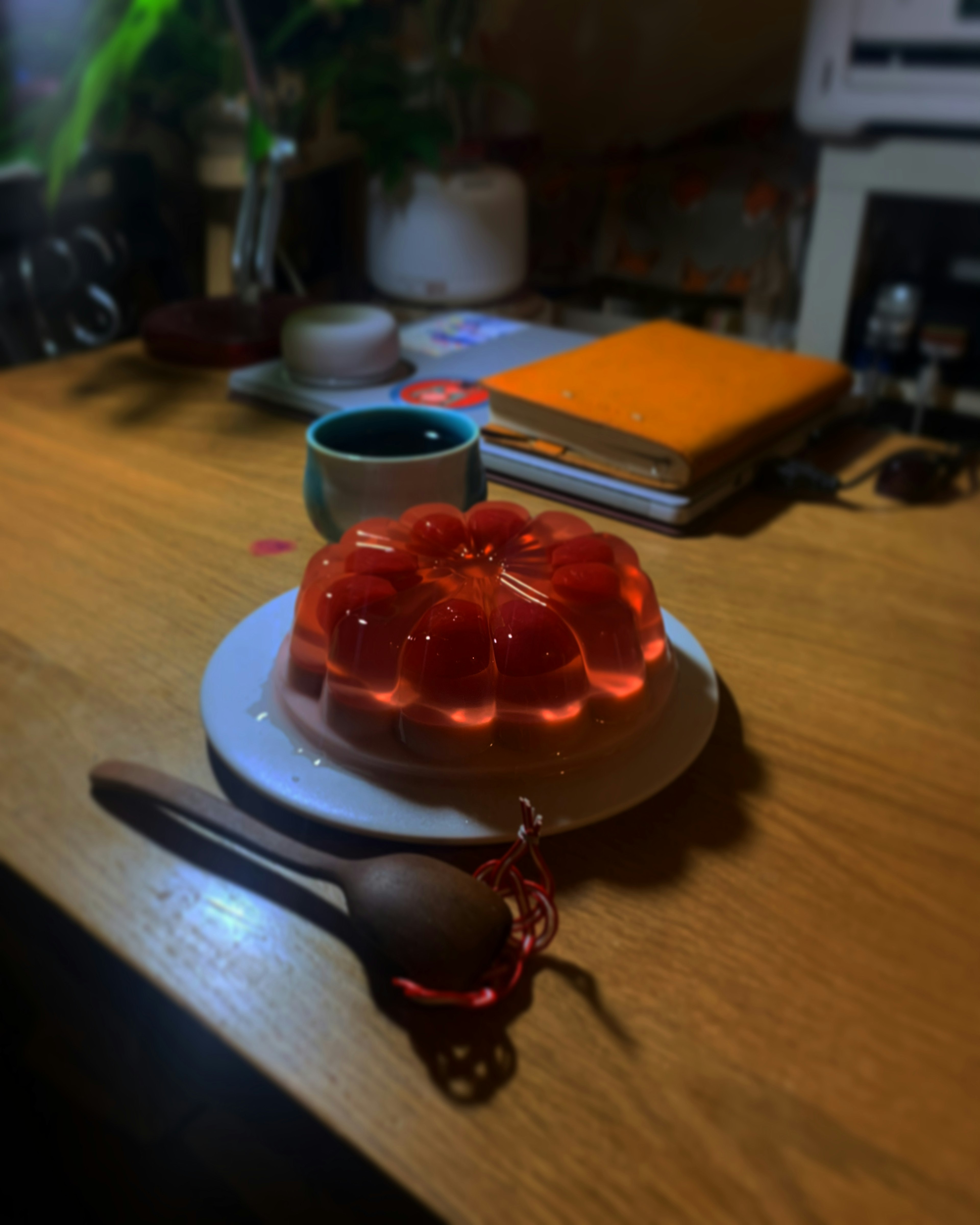 Red jelly on a white plate with a wooden spoon warm drink and books in the background