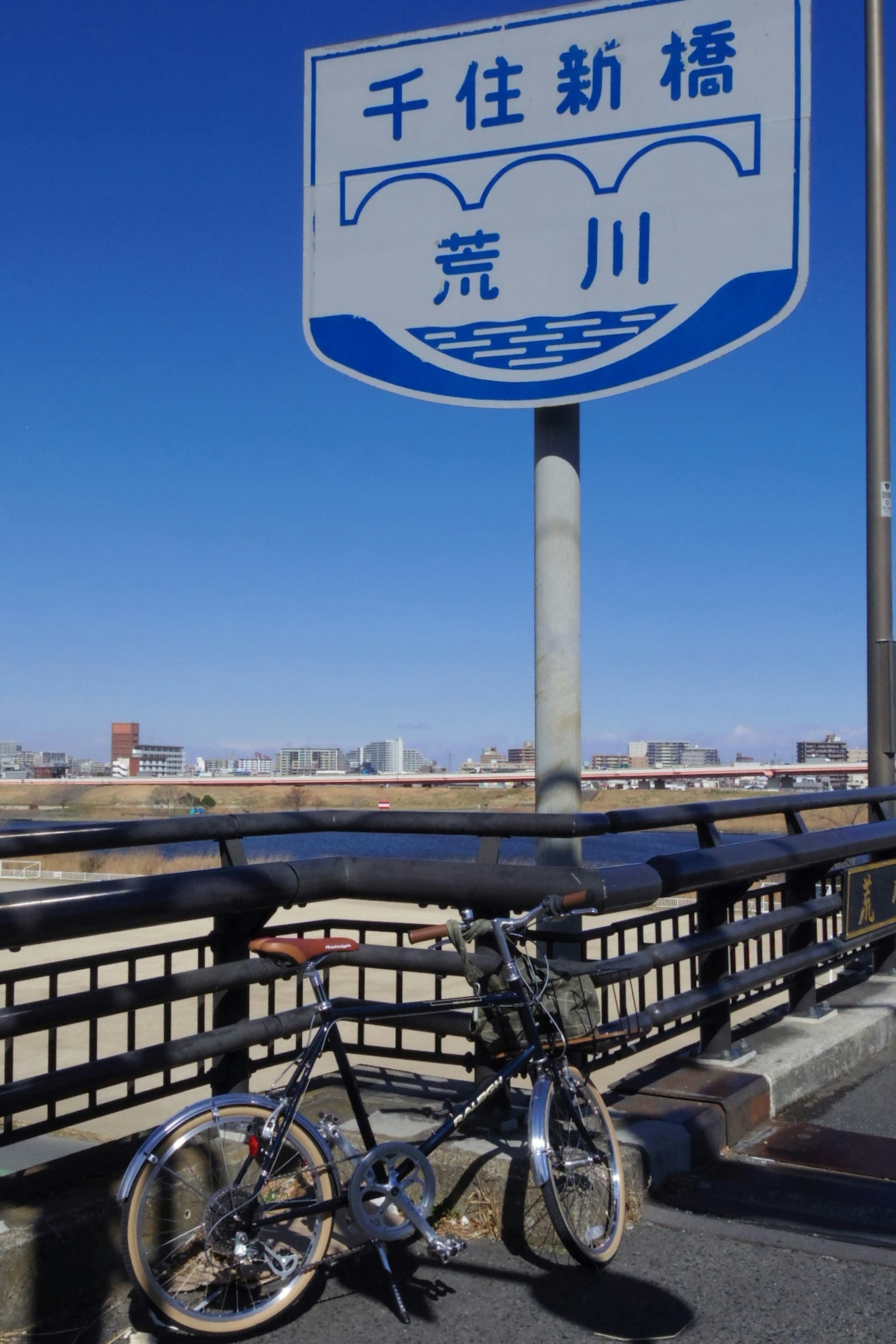 Schild für Senju Shimbashi über dem Arakawa-Fluss mit einem Fahrrad