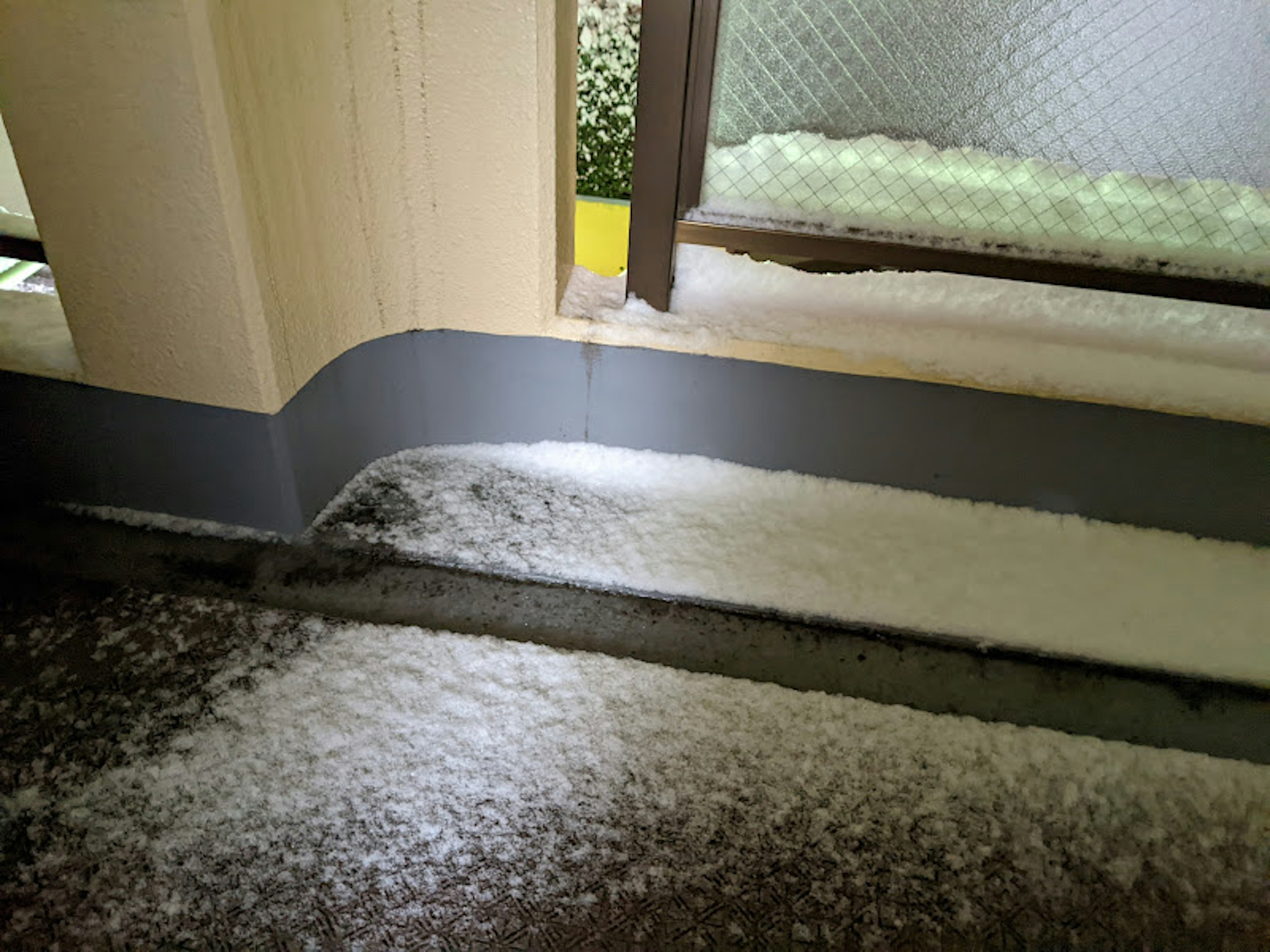 Primer plano de pellets de hielo que parecen nieve en el suelo cerca de una ventana