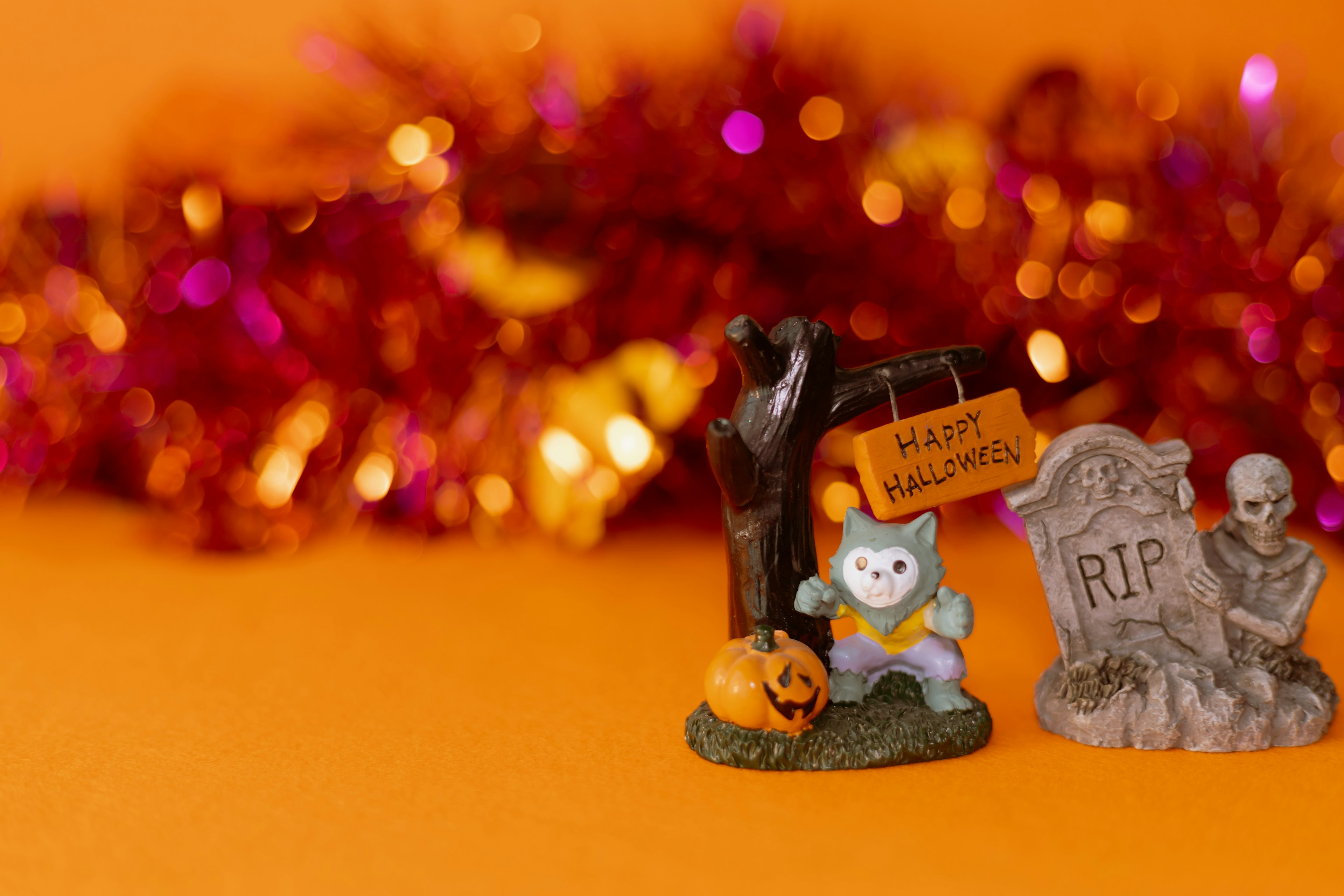 Halloween decorations on an orange background featuring a cat figurine a jack-o-lantern and a gravestone