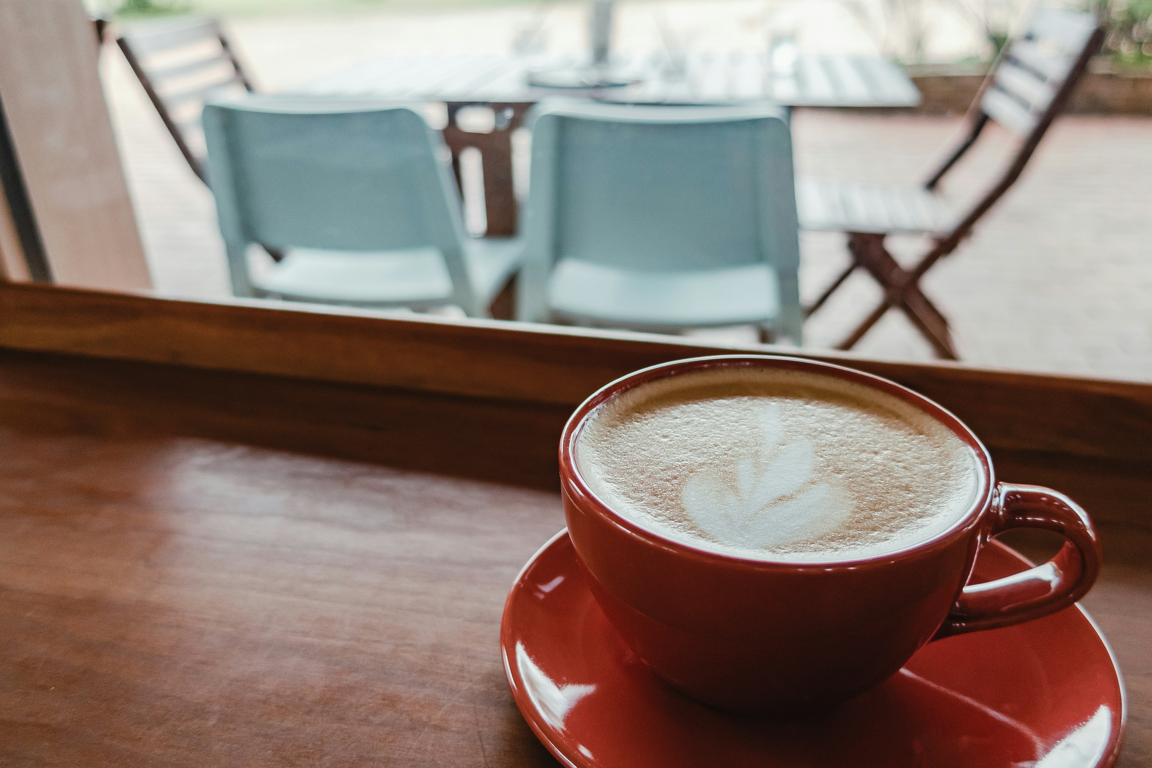 Un café con arte latte en una taza roja sobre una mesa de madera en una cafetería