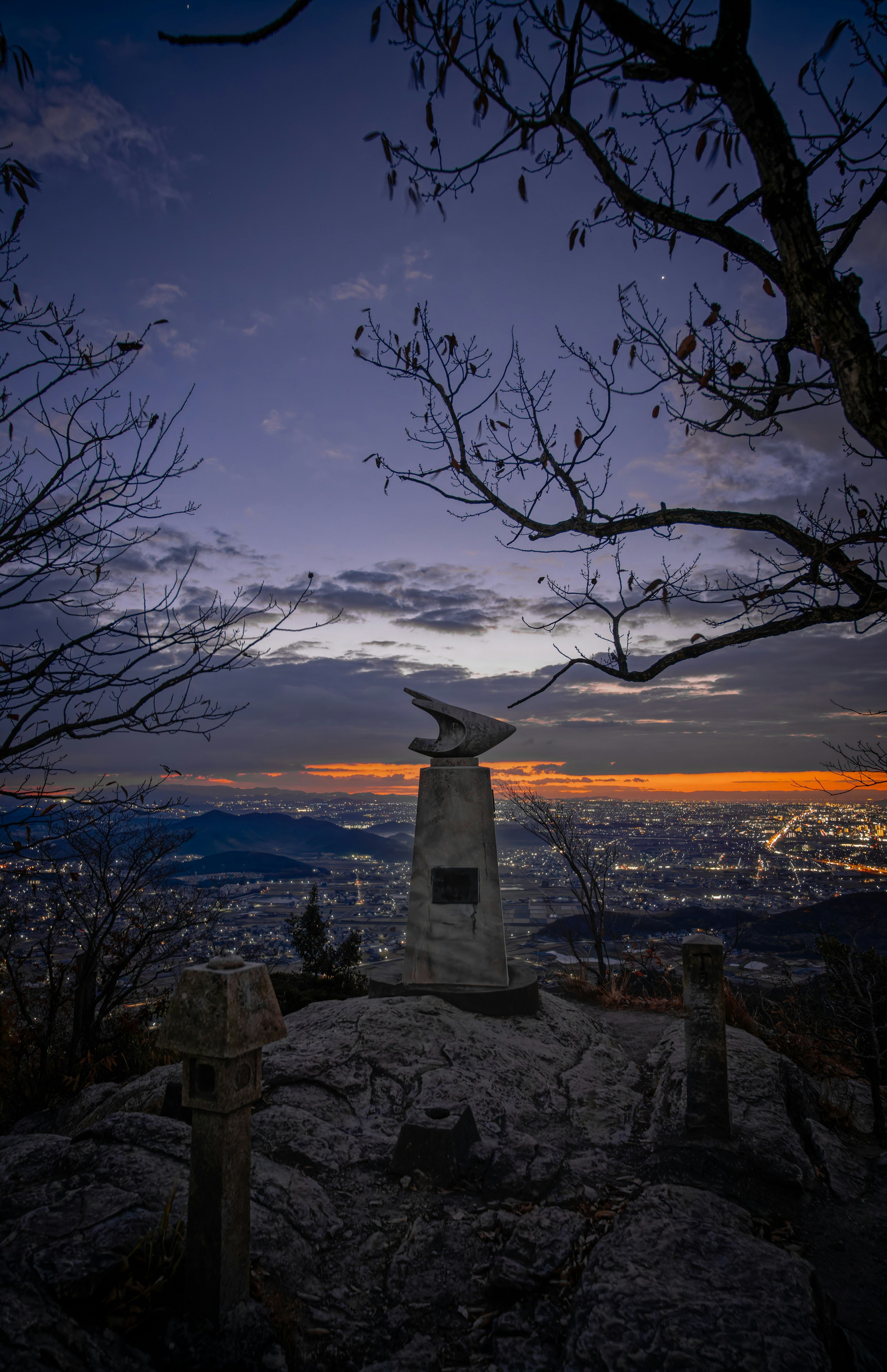 夕焼けの空を背景にした山頂の記念碑と周囲の風景