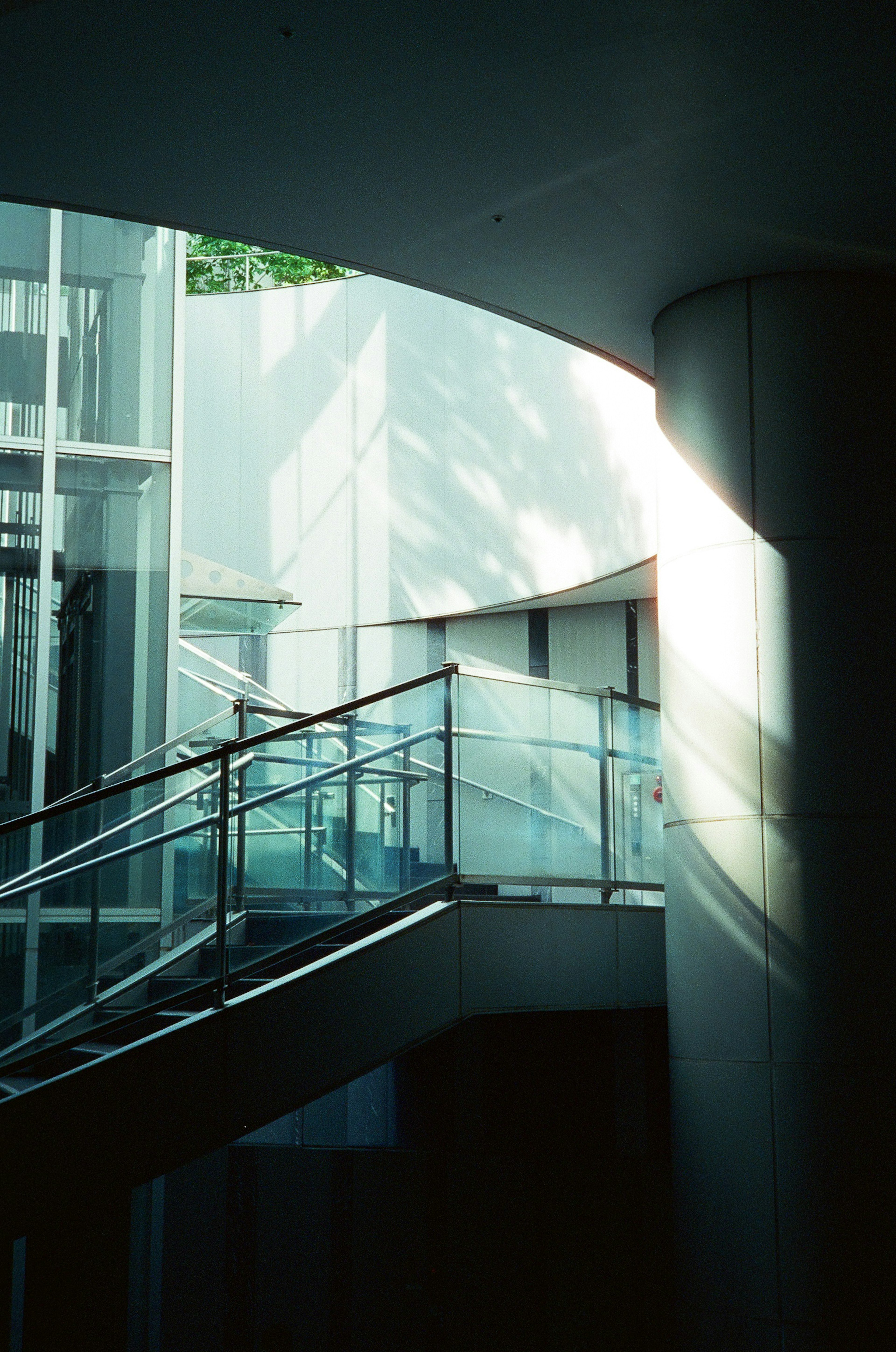 Vista interior de una escalera curva con paredes blancas y barandilla de vidrio