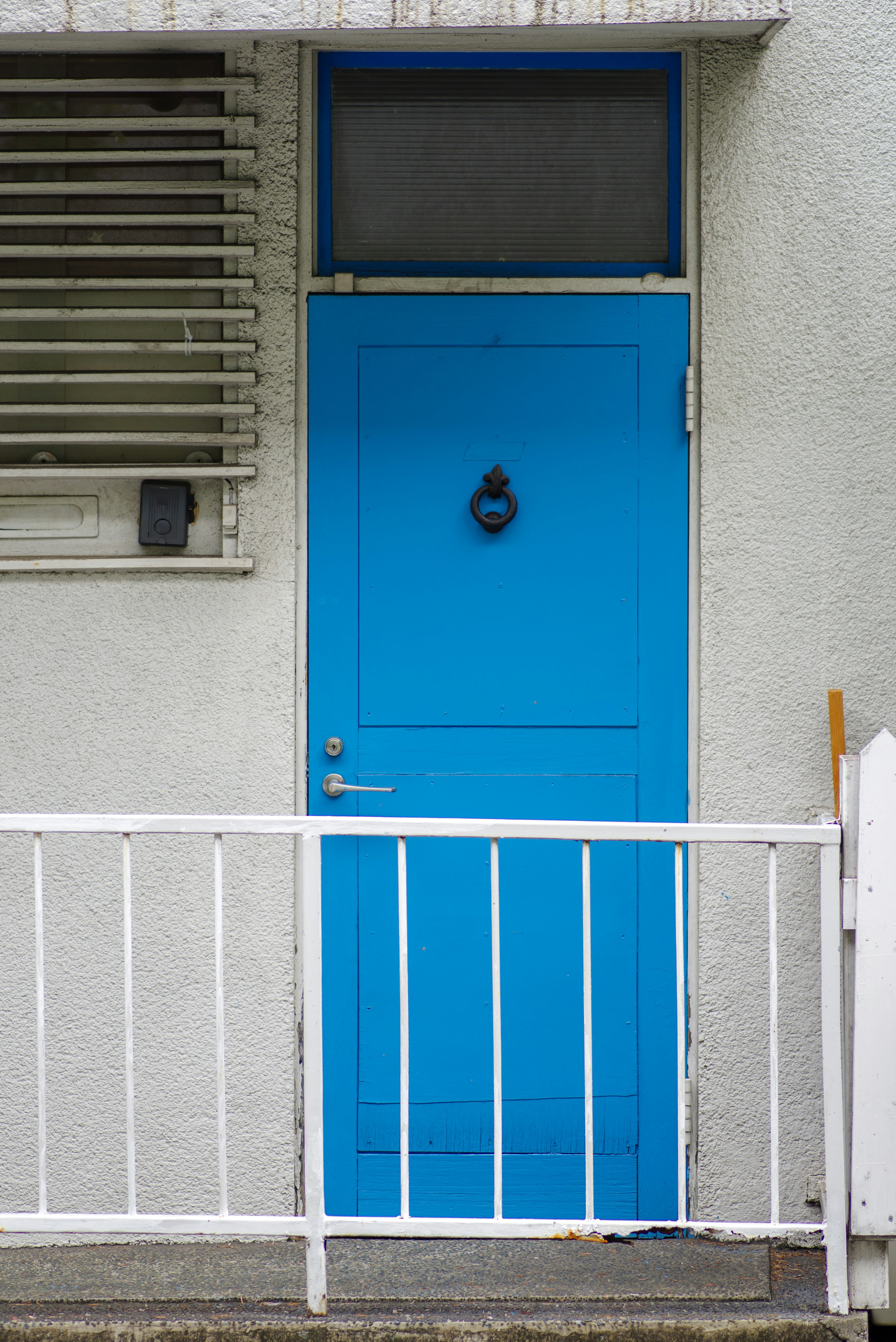 Vibrant blue door with a unique knocker and white railing in front of a building