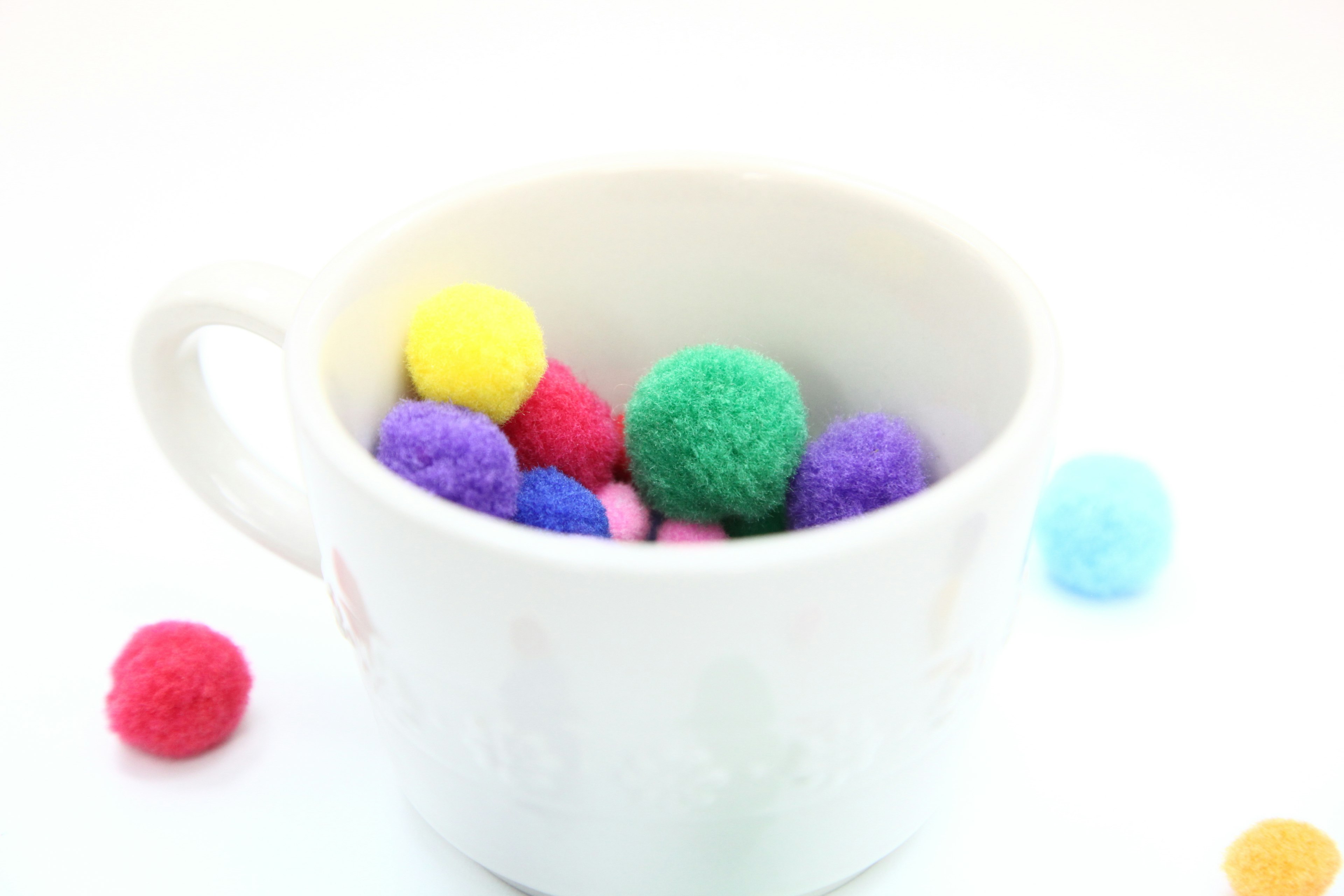 Colorful pom poms inside a white cup with some scattered around