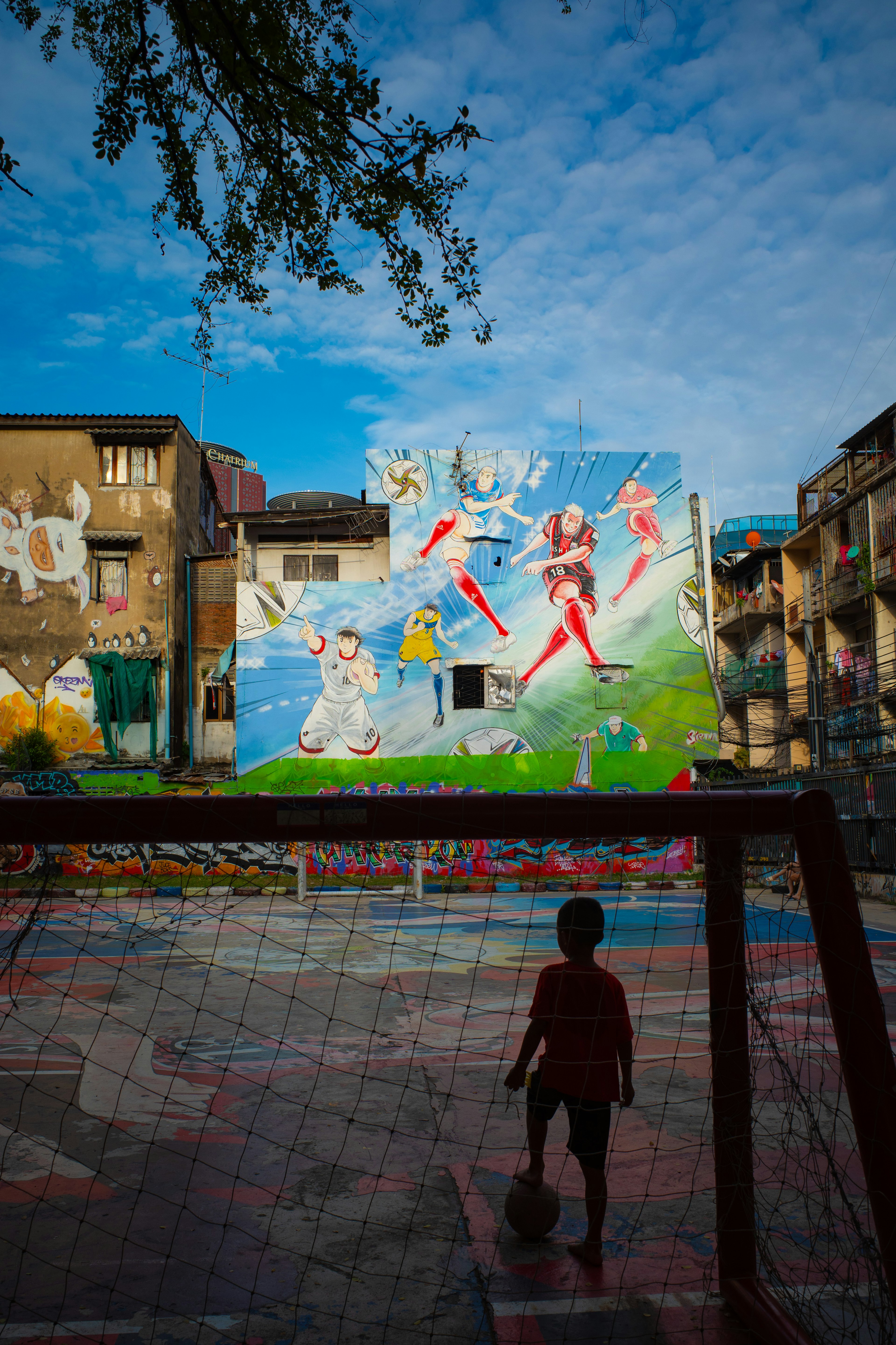 Niño de pie frente a una portería de fútbol con un mural colorido al fondo