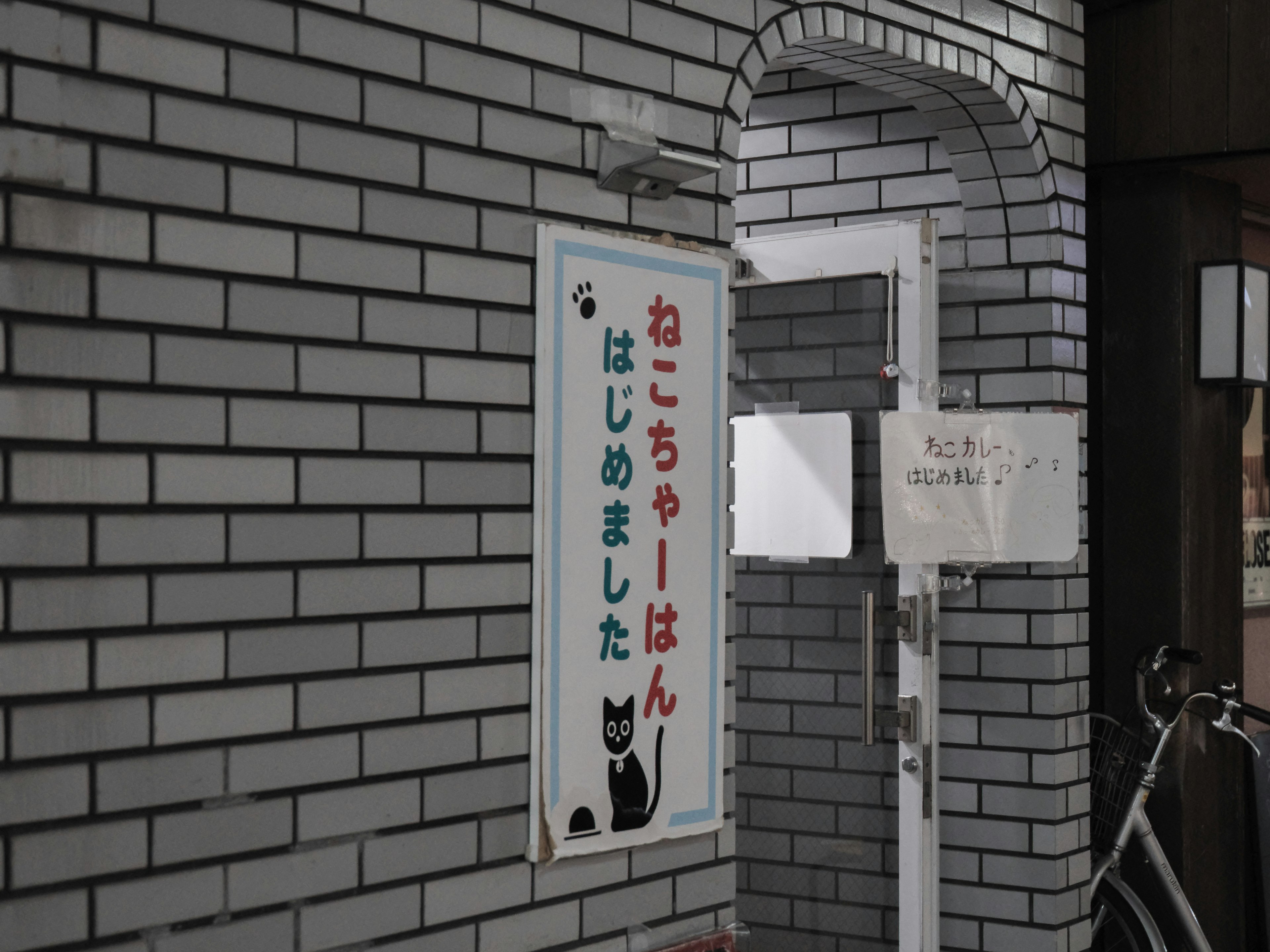 A sign featuring a black cat illustration on a white brick wall