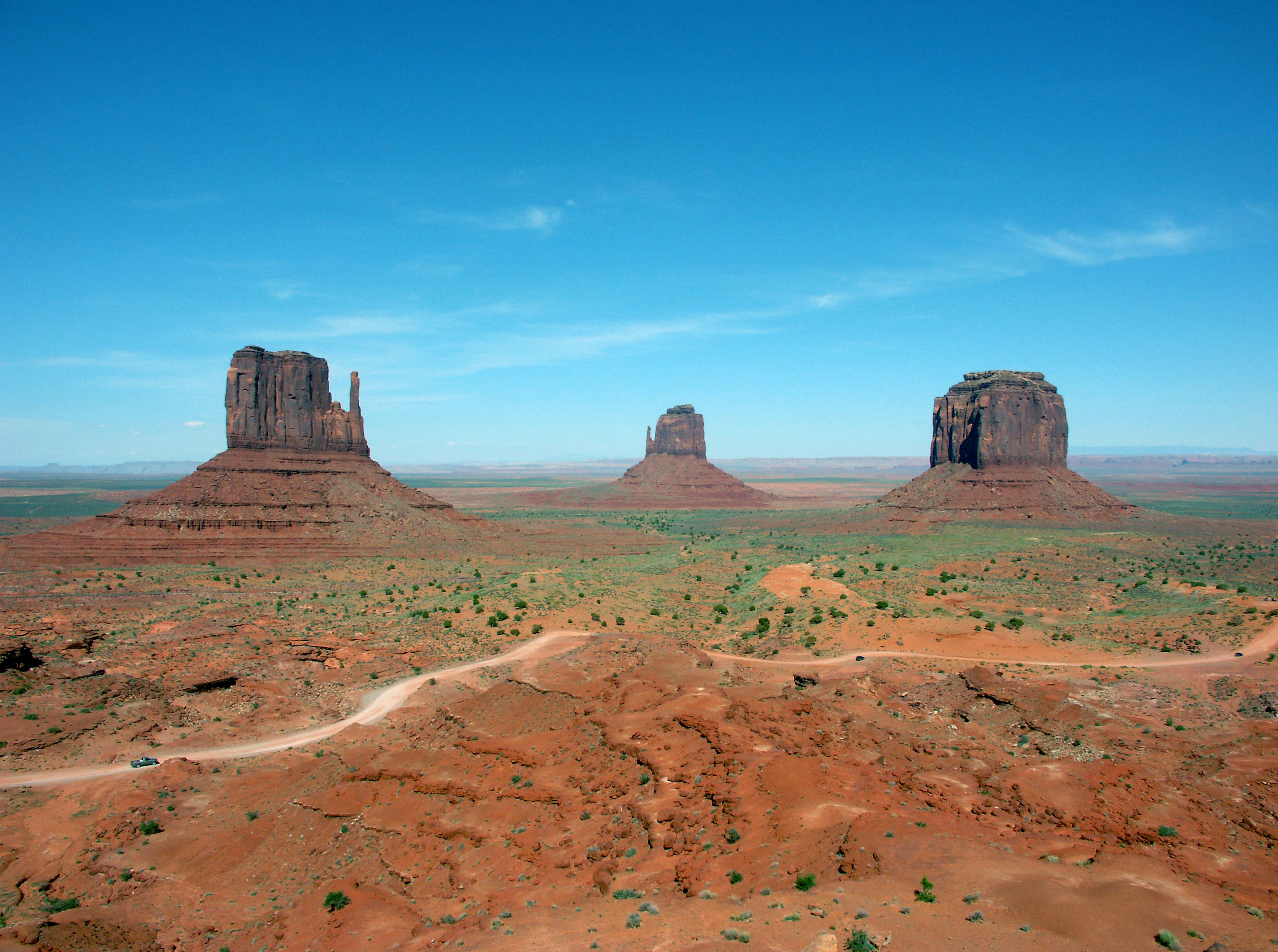 Landschaft des Monument Valley mit drei Felsformationen blauem Himmel und roter Erde